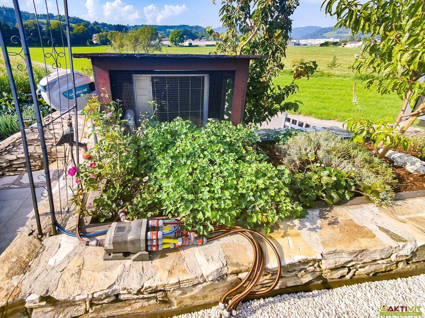 Gartenbereich mit Bewässerungssystem, einem kleinen Tiergehege und einer Natursteinmauer.