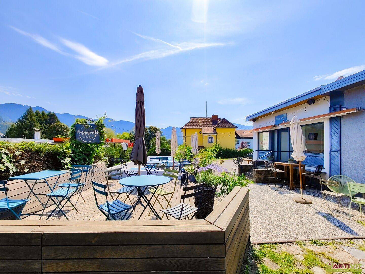 Geräumige Holzterrasse mit verschiedenen Sitzgelegenheiten und Sonnenschirmen, umgeben von grüner Landschaft.