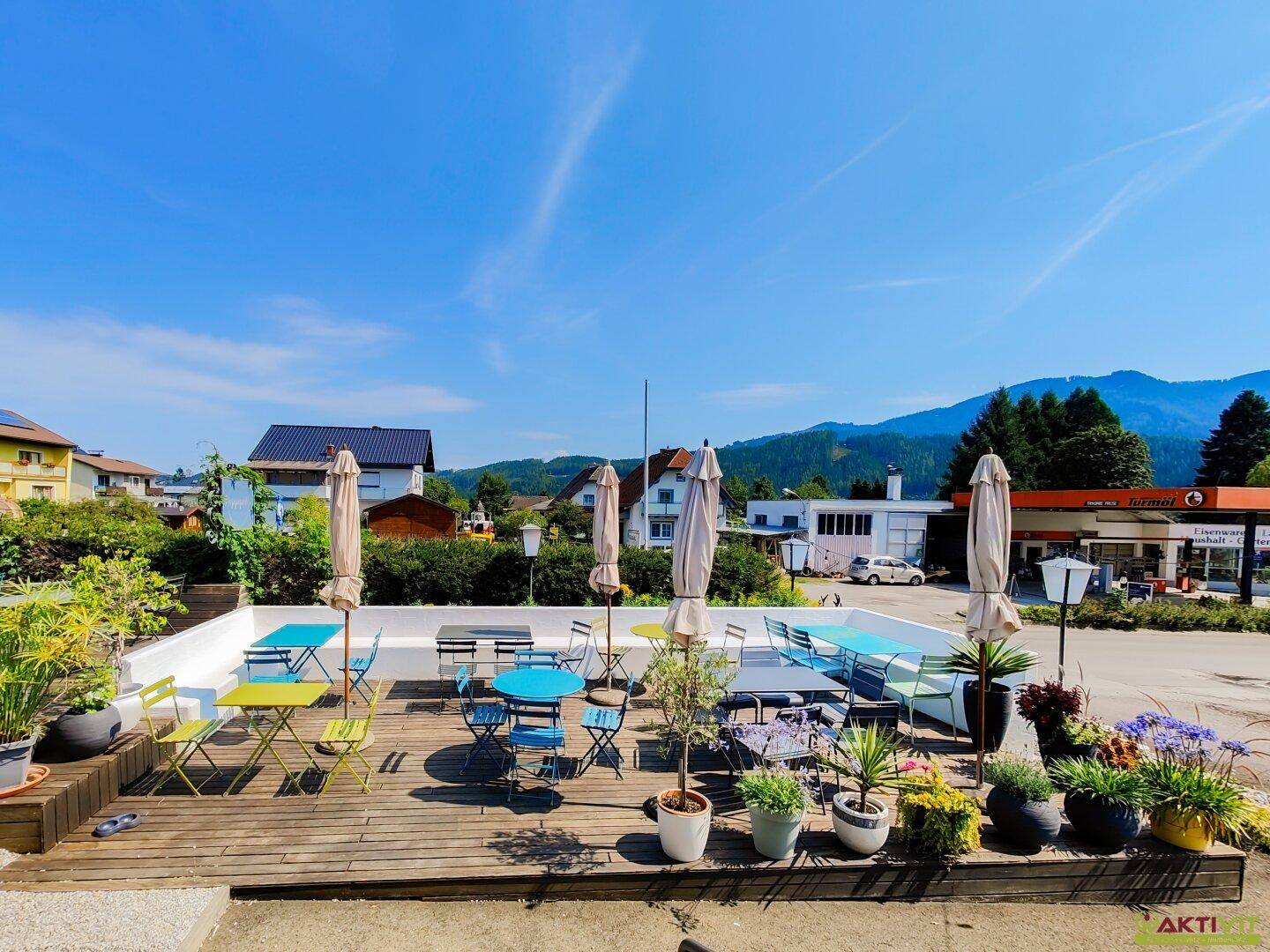 Weitläufige Holzterrasse mit bunten Möbeln und Sonnenschirmen, bietet einen weiten Blick auf die Umgebung.