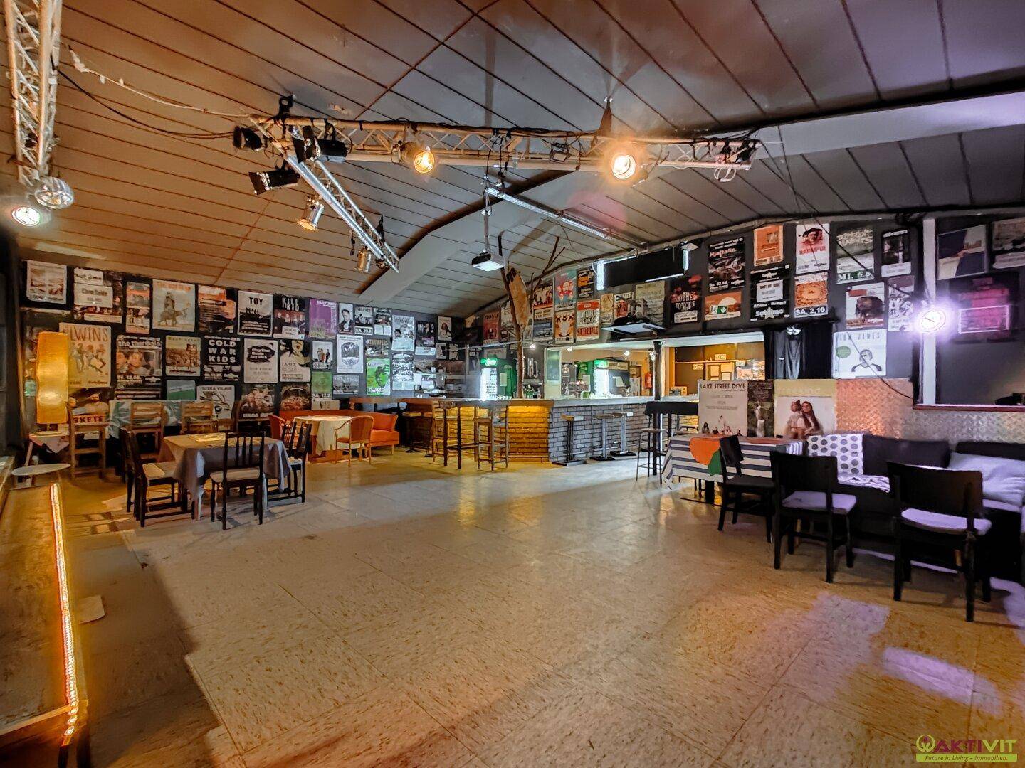 Weitläufiger Veranstaltungsraum mit Bühne und Bar im Hintergrund, ideal für größere Events.