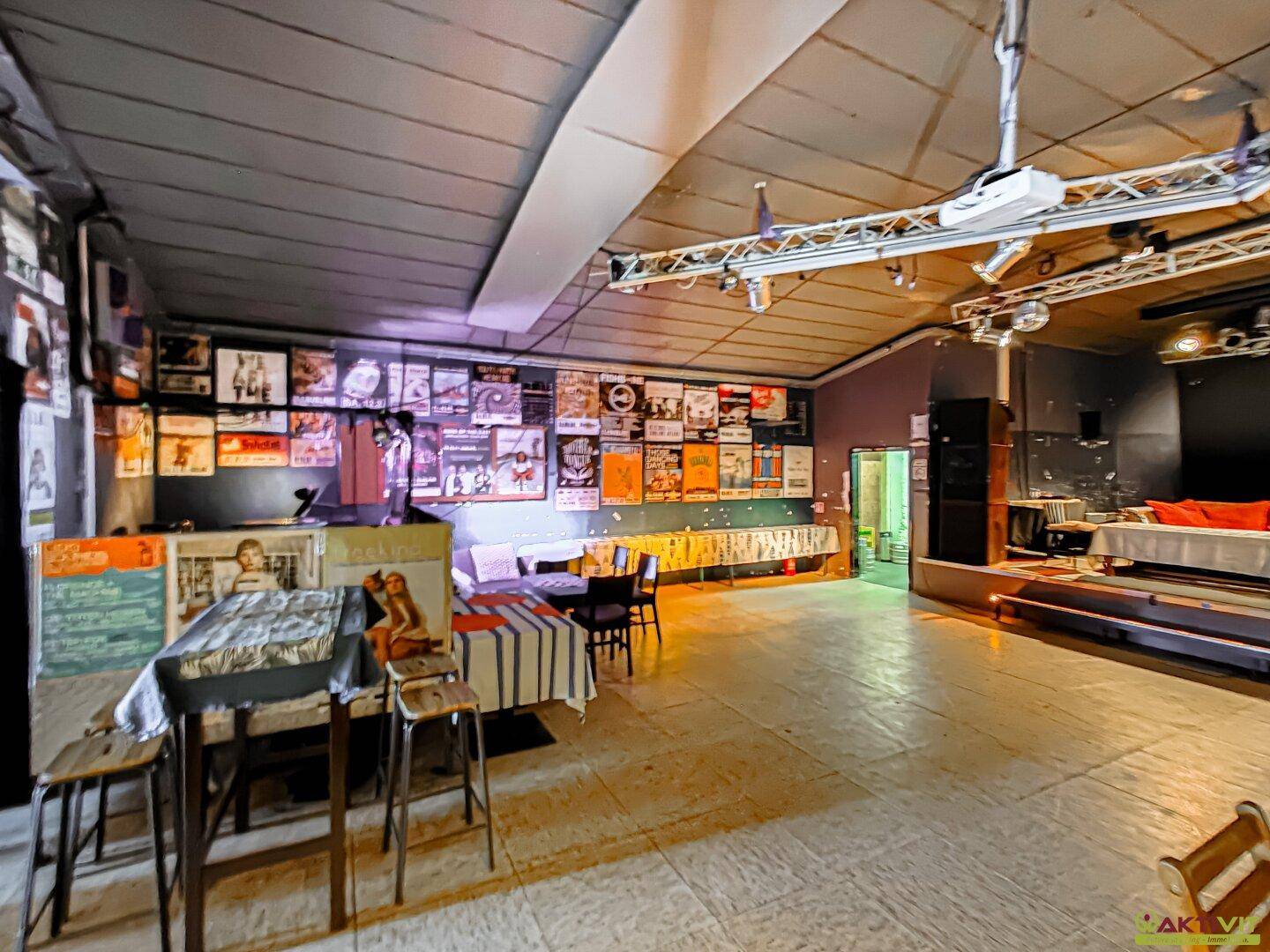 Großer Saal mit Bühne und vielen Postern an den Wänden, bietet Platz für diverse Veranstaltungen.