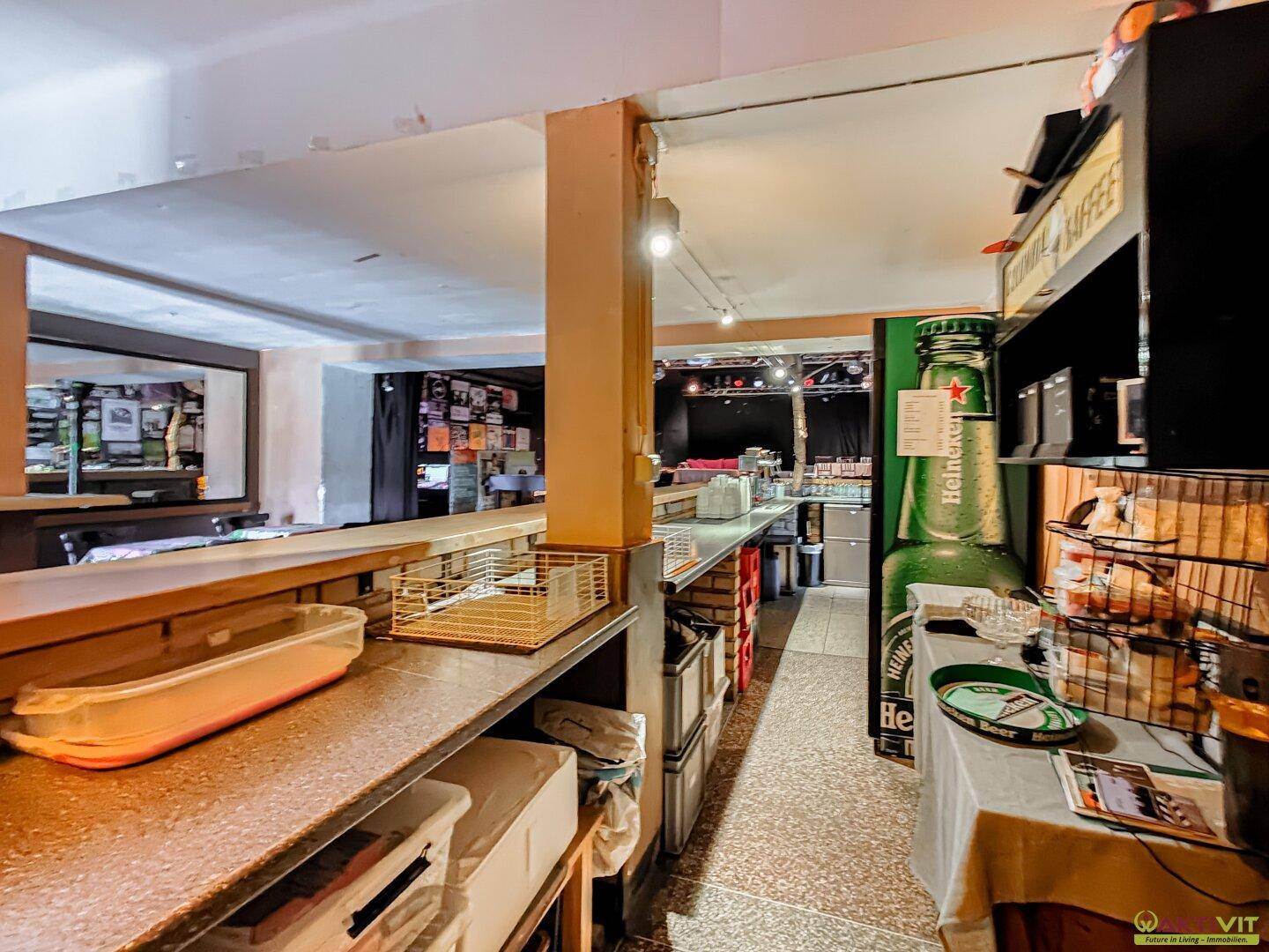 Bar-Bereich mit Theke, Regalen und einer großen Heineken-Flasche, die auf einen Veranstaltungsraum oder eine Gaststätte hinweist.