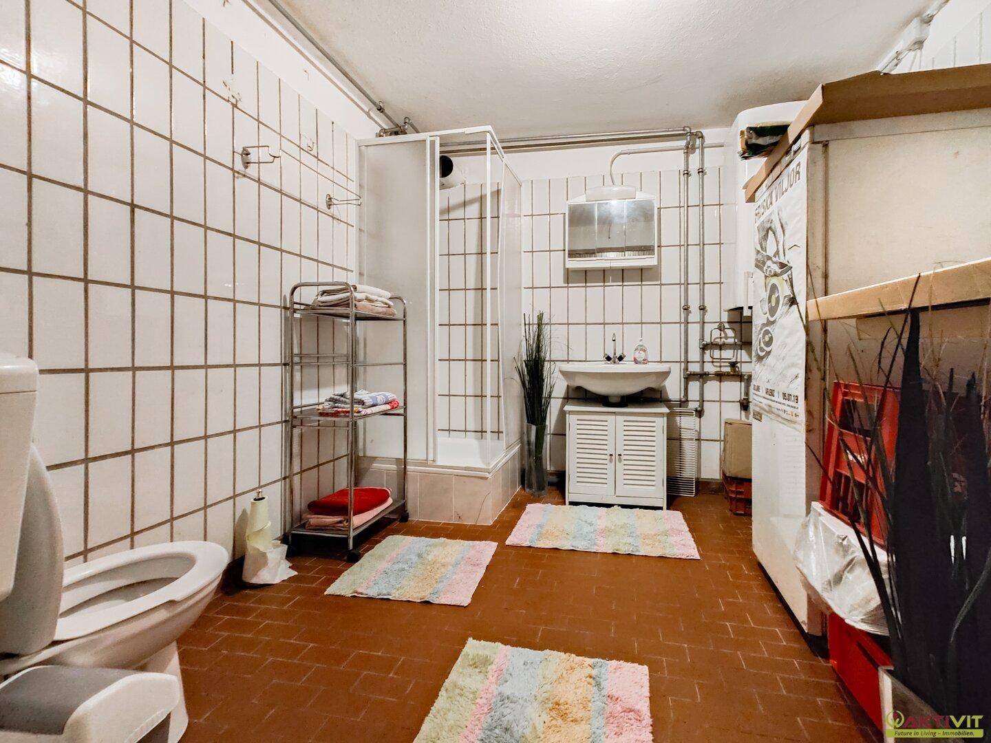 Funktionales Badezimmer mit Toilette, Duschkabine und Waschbecken, ausgestattet mit weißen Wandfliesen und Terrakotta-Bodenfliesen.