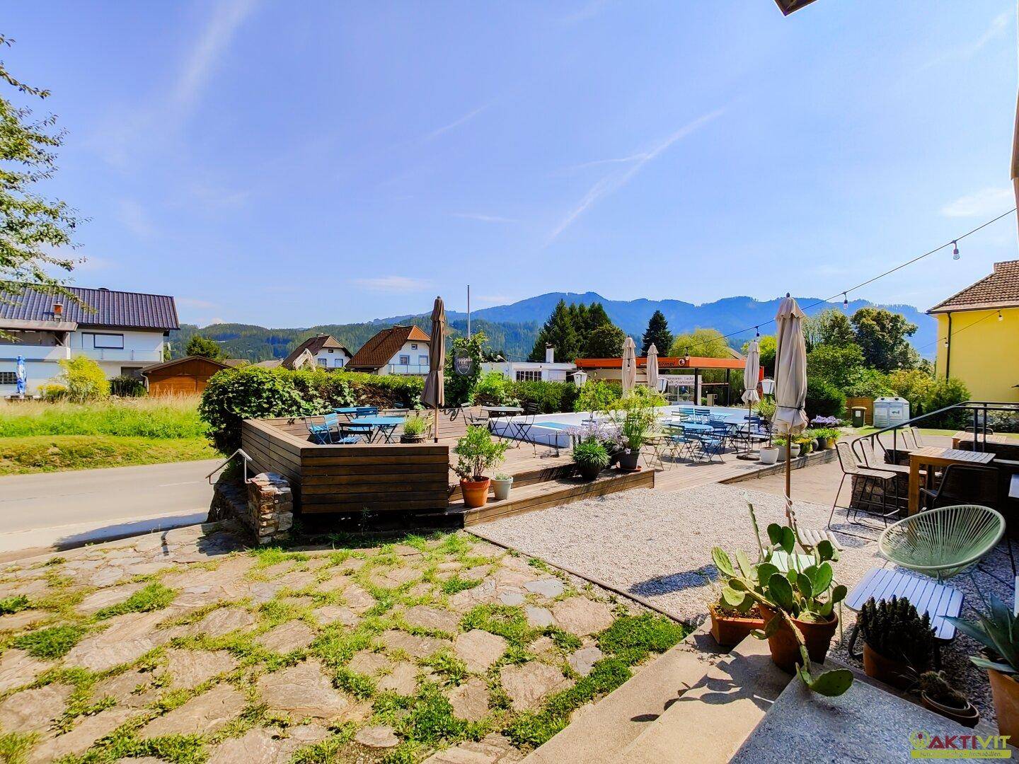 Große Außenterrasse mit Tischen, Stühlen und Sonnenschirmen, die einen weiten Blick auf die umliegende Landschaft und Berge bietet.