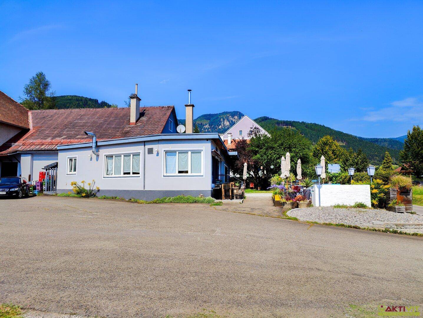 Außenansicht des Gebäudes mit Parkplatz und der umliegenden Landschaft, im Hintergrund sind Berge zu sehen.