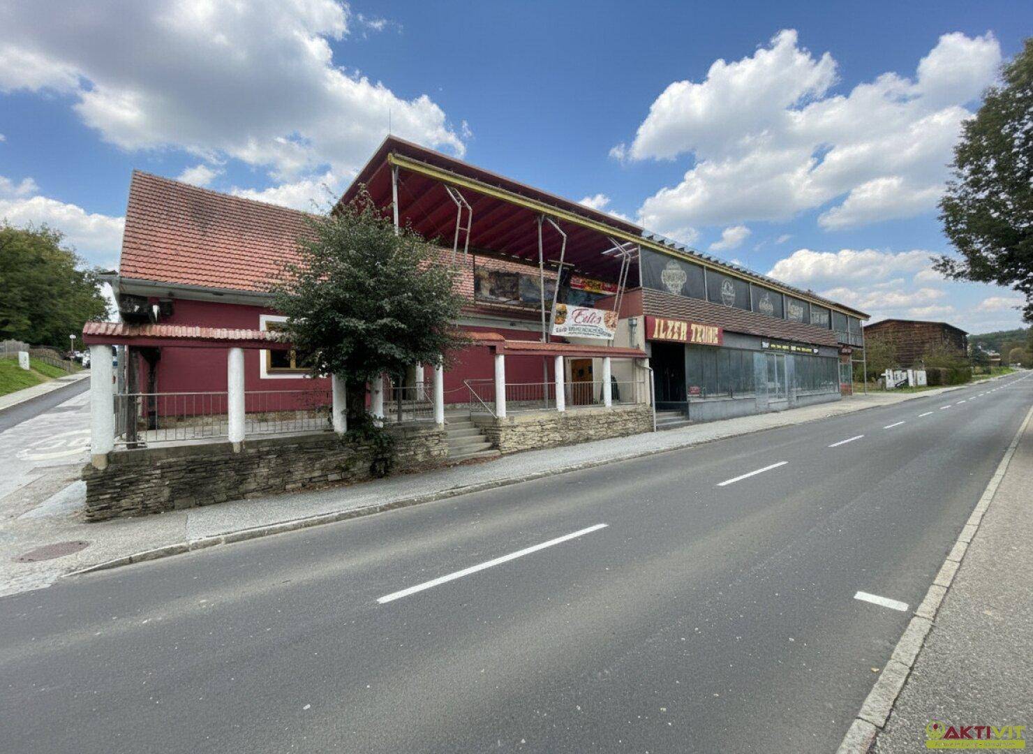Seitenansicht des Gebäudes mit rotem Ziegeldach und einer erhöhten Terrasse entlang der Fassade.