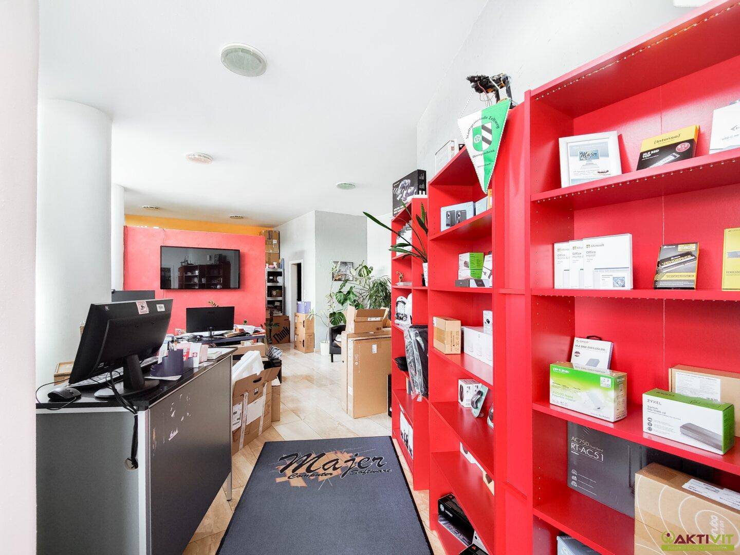 Langer Bürobereich mit roten Regalen, Arbeitsplätzen und einem Teppichläufer.