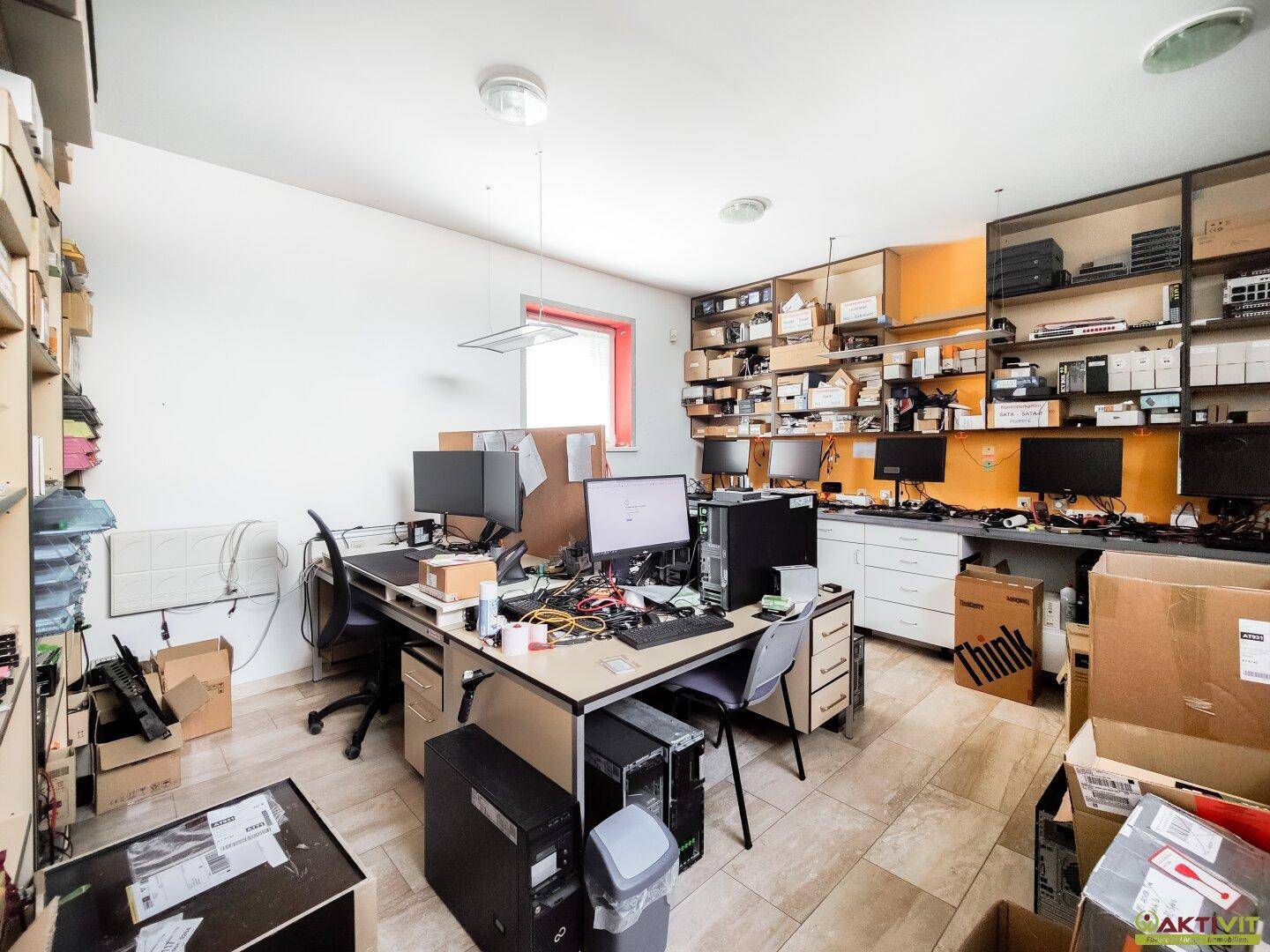 Organisiertes Büro mit mehreren Computern, Regalen und orangefarbener Akzentwand.