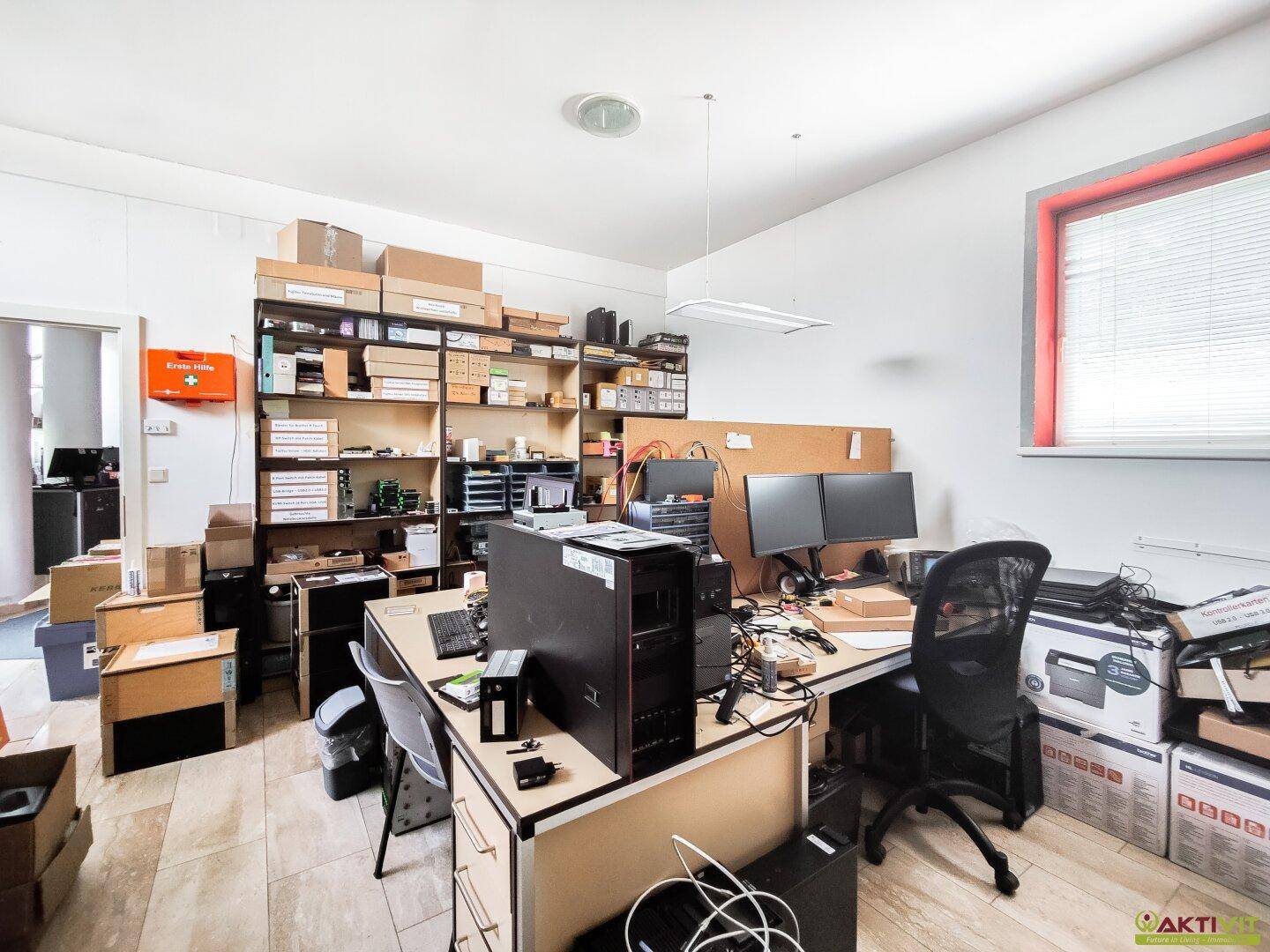 Funktionaler Bürobereich mit Schreibtischen, Computern und Regalen für Lagerung.