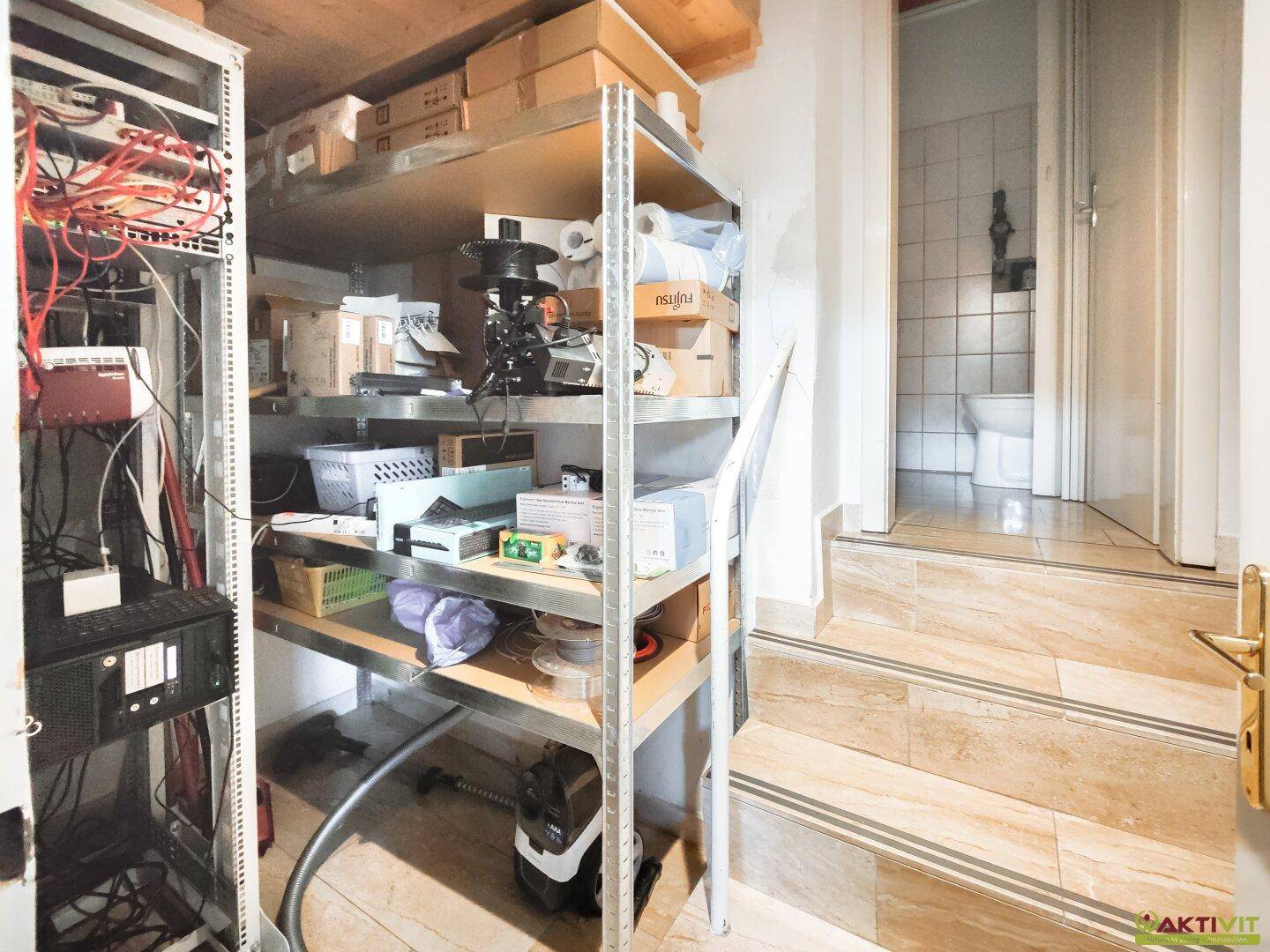 Lagerbereich mit Regalen und Serverracks, führt zu einem gefliesten Badezimmer.