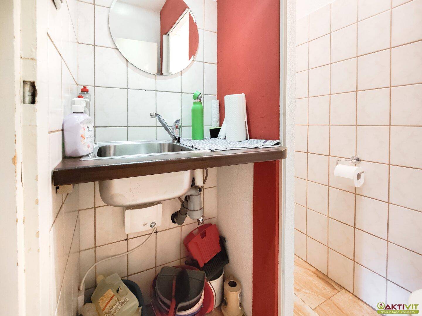 Kleines Badezimmer mit Waschbecken, Spiegel und roten Akzentwänden, einfach gefliest.