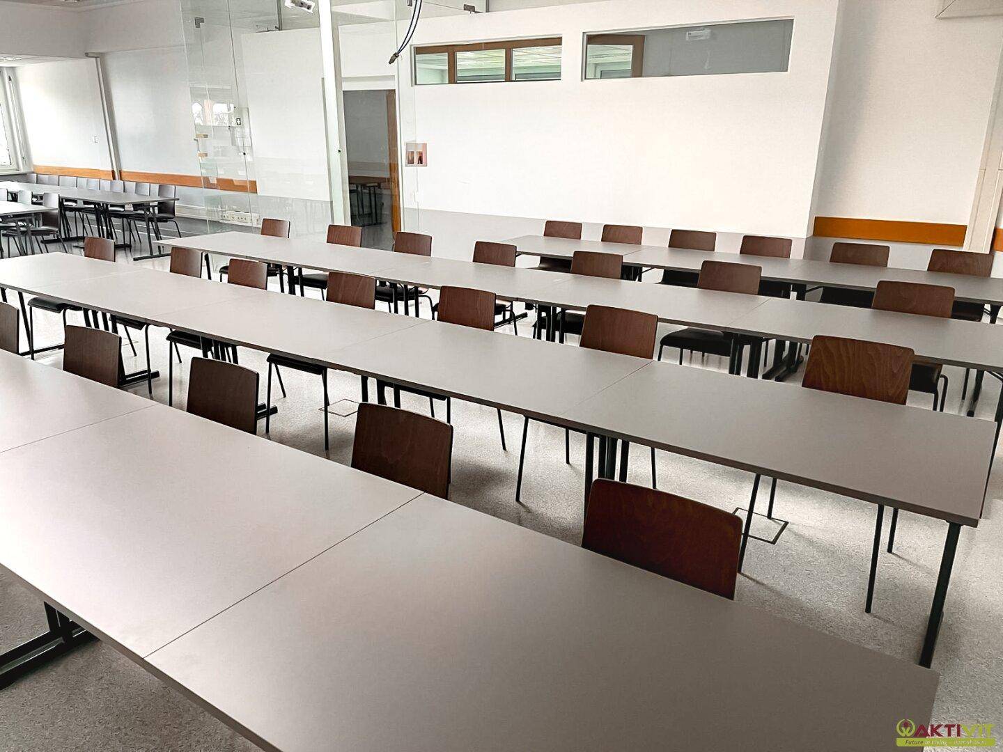 Weitläufiger Schulungsraum mit flexibler Bestuhlung und Tischen, durch eine Glaswand abgetrennt, mit viel Tageslicht und Fliesenboden.