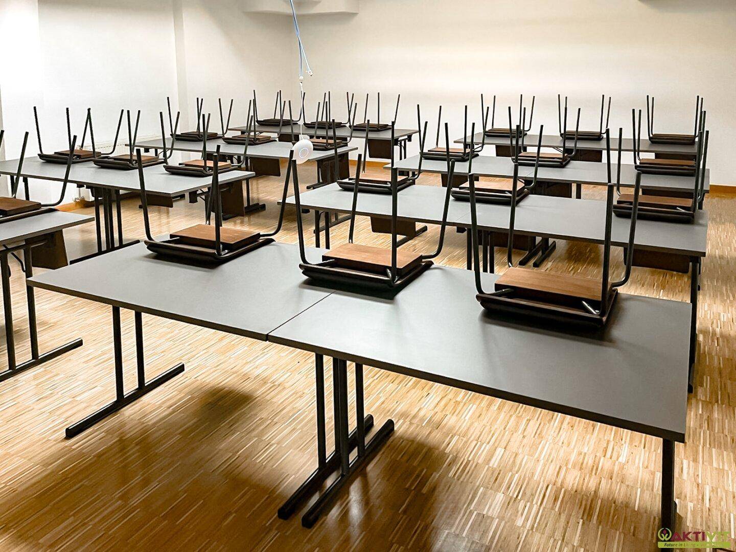 Schulungsraum mit auf Tischen gestapelten Stühlen, bereit zur Reinigung, mit hellem Holzfußboden und Deckenbeleuchtung.