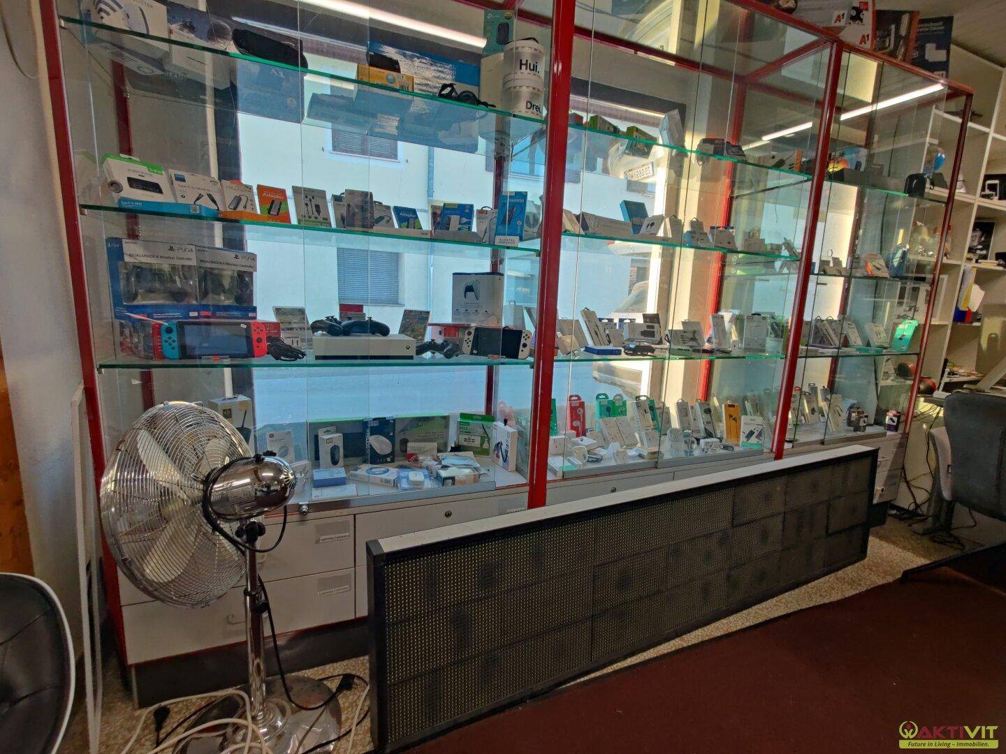 Große Glasvitrine mit einer Vielzahl von Elektronikartikeln und Zubehör, beleuchtet und gut sichtbar präsentiert.
