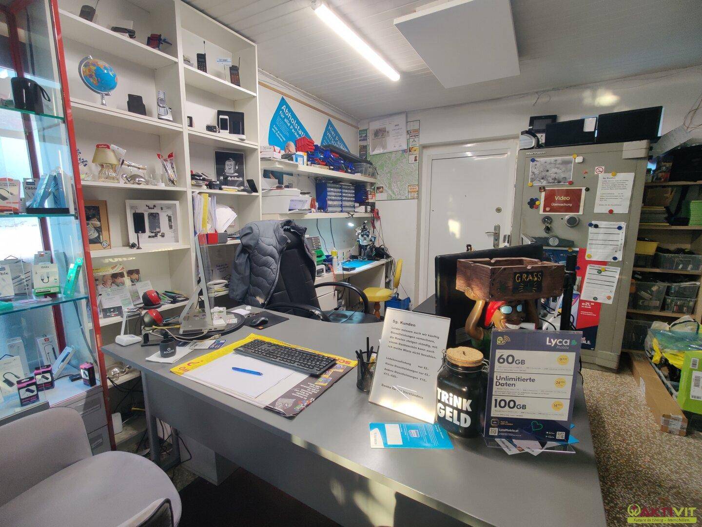 Büro- oder Werkstattbereich mit Schreibtisch, Computer, Regalen und Werkzeugen für Reparaturen und Verwaltung.