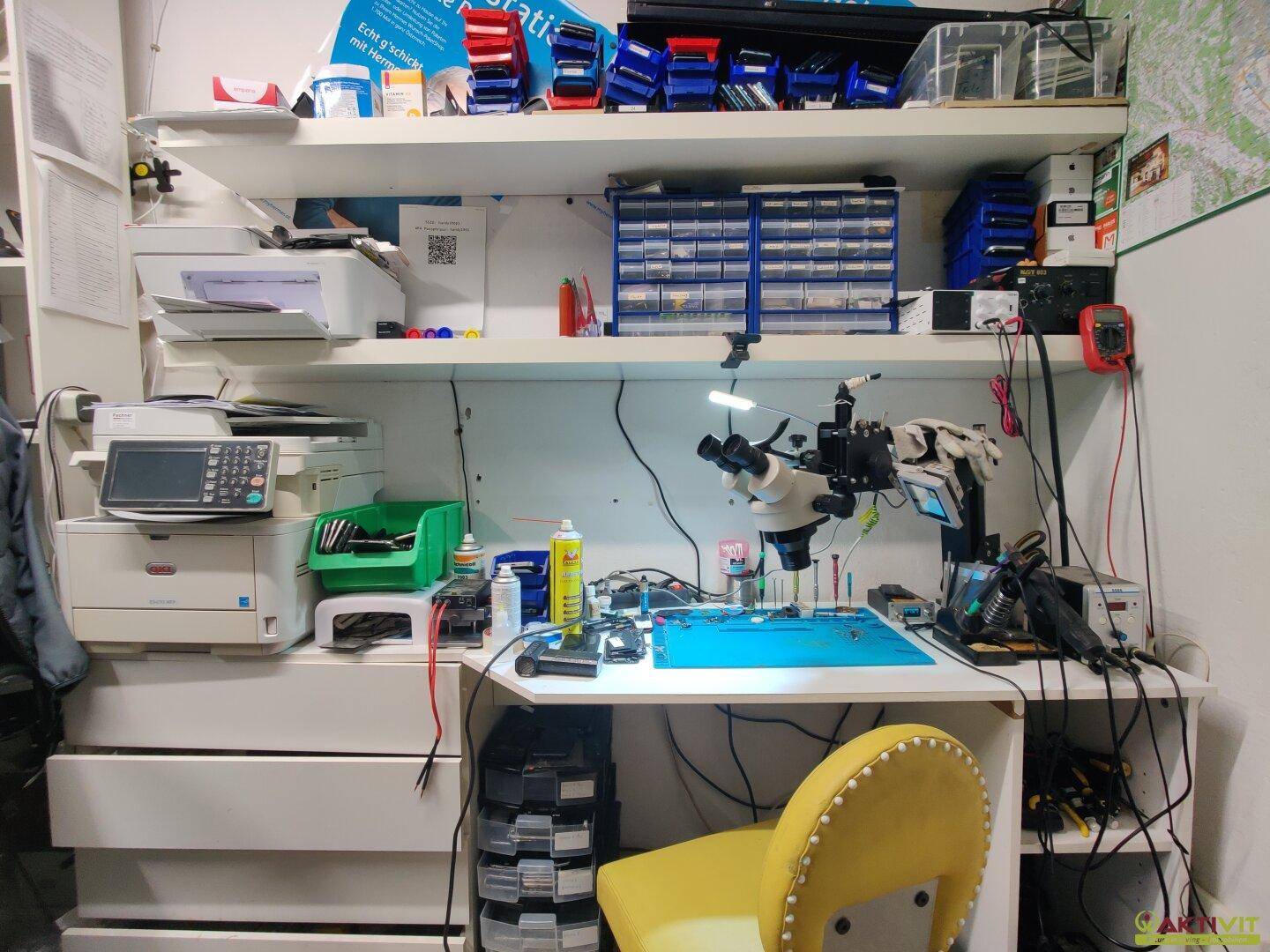 Detaillierter Blick auf einen Werkstattbereich mit Mikroskop, Werkzeugen und elektronischen Geräten für Reparaturen.