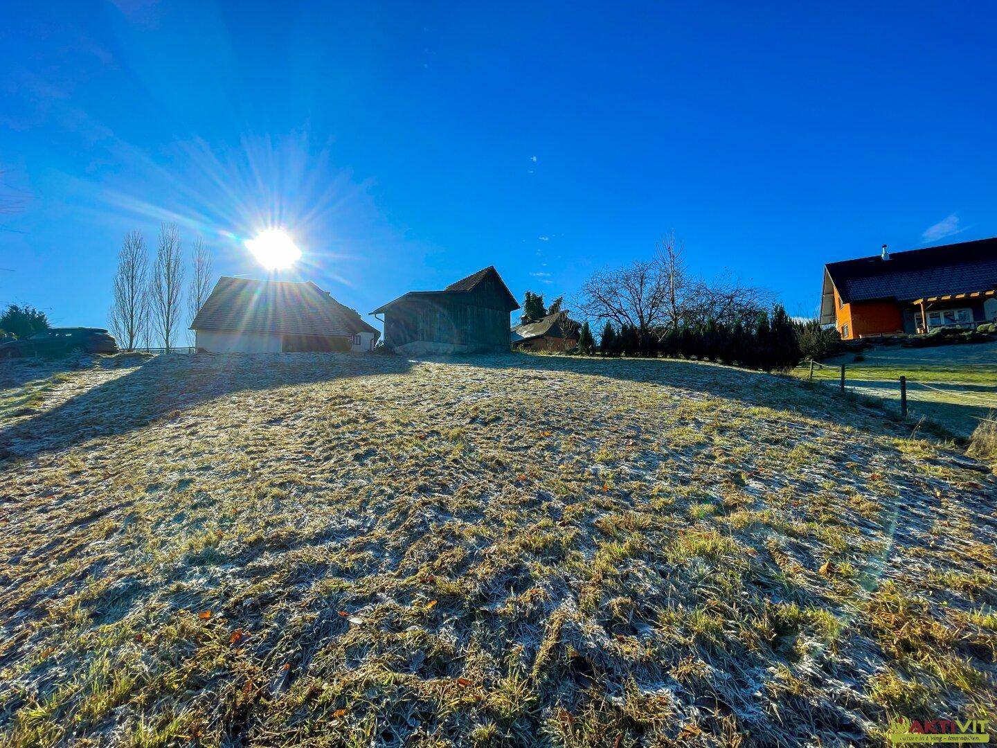 Sonniges, frostbedecktes Hügelgelände mit mehreren Gebäuden in der Ferne und strahlendem Himmel.