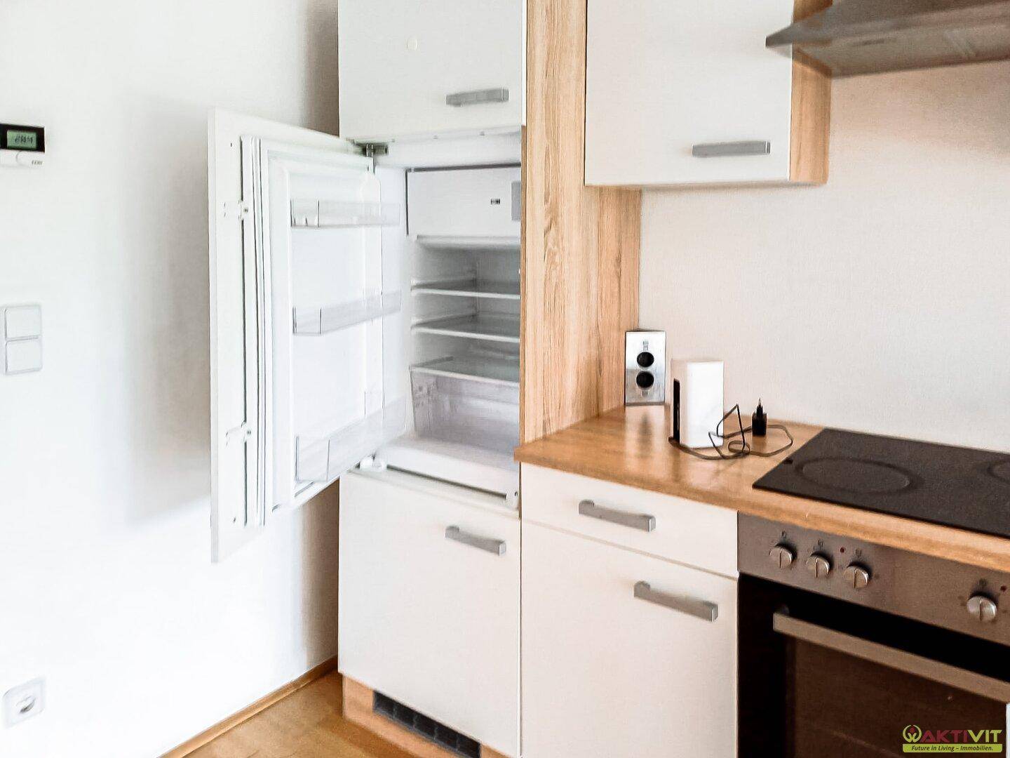 Moderne Einbauküche mit weißen Schränken, Holztheke und integriertem Kühlschrank.