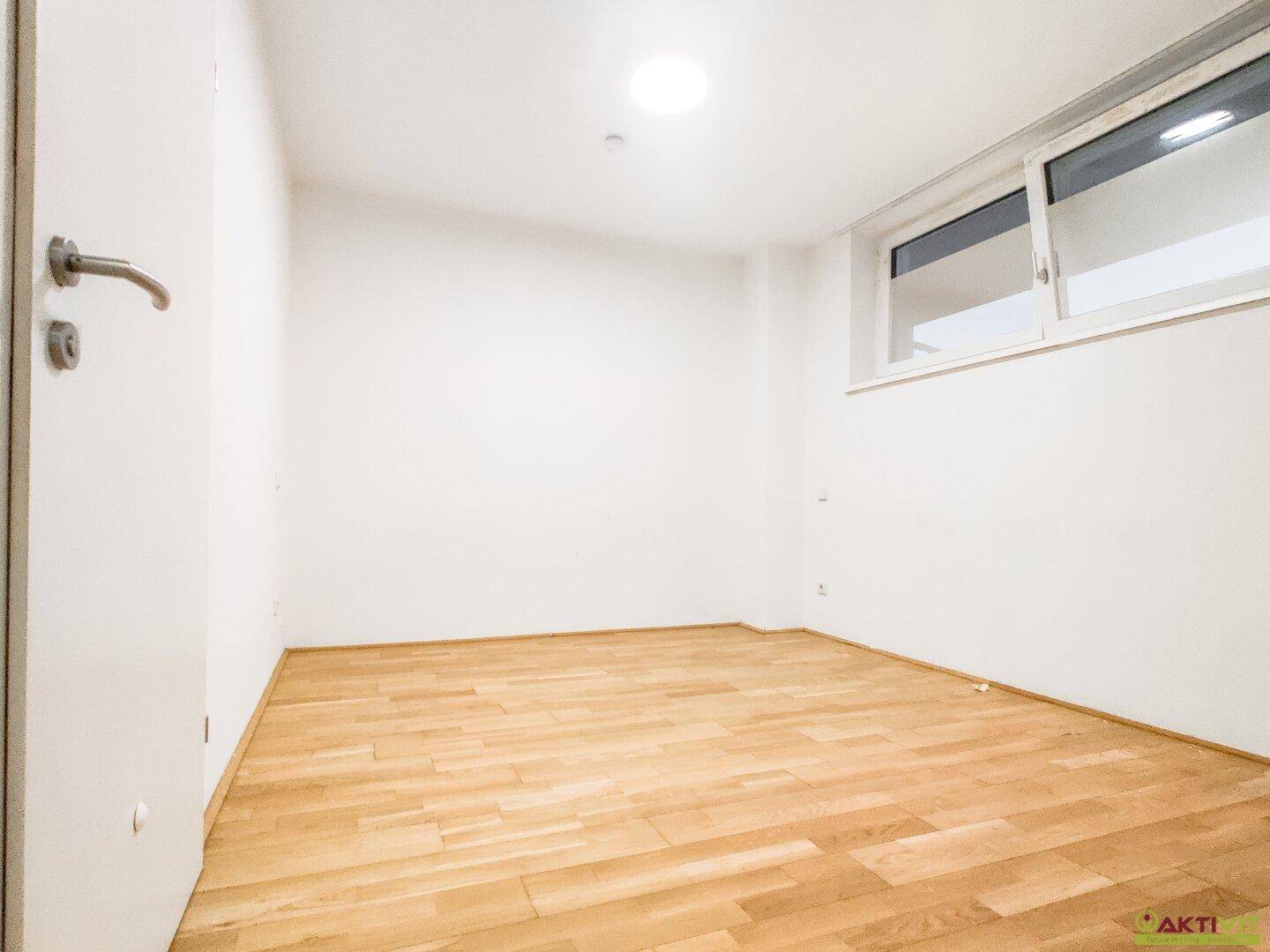 Leeres Zimmer mit hellem Parkettboden und einem Fenster, ideal als Schlaf- oder Arbeitszimmer.
