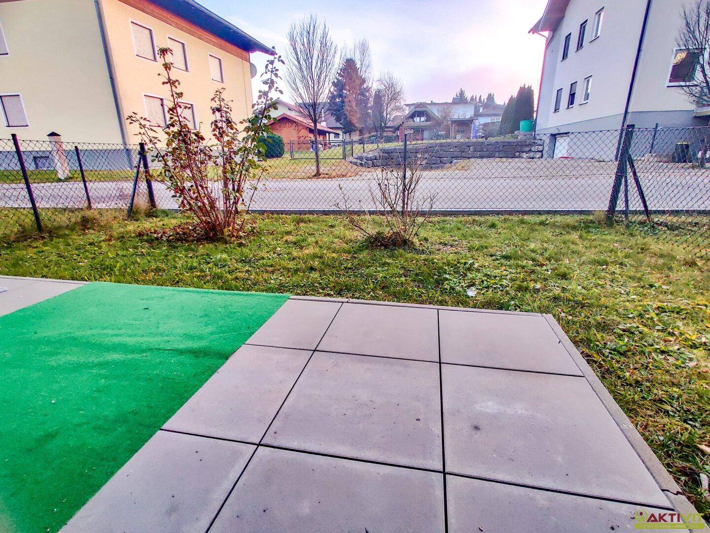 Kleine gepflasterte Terrasse mit Kunstrasen und Blick auf die umliegenden Häuser und Grünflächen.