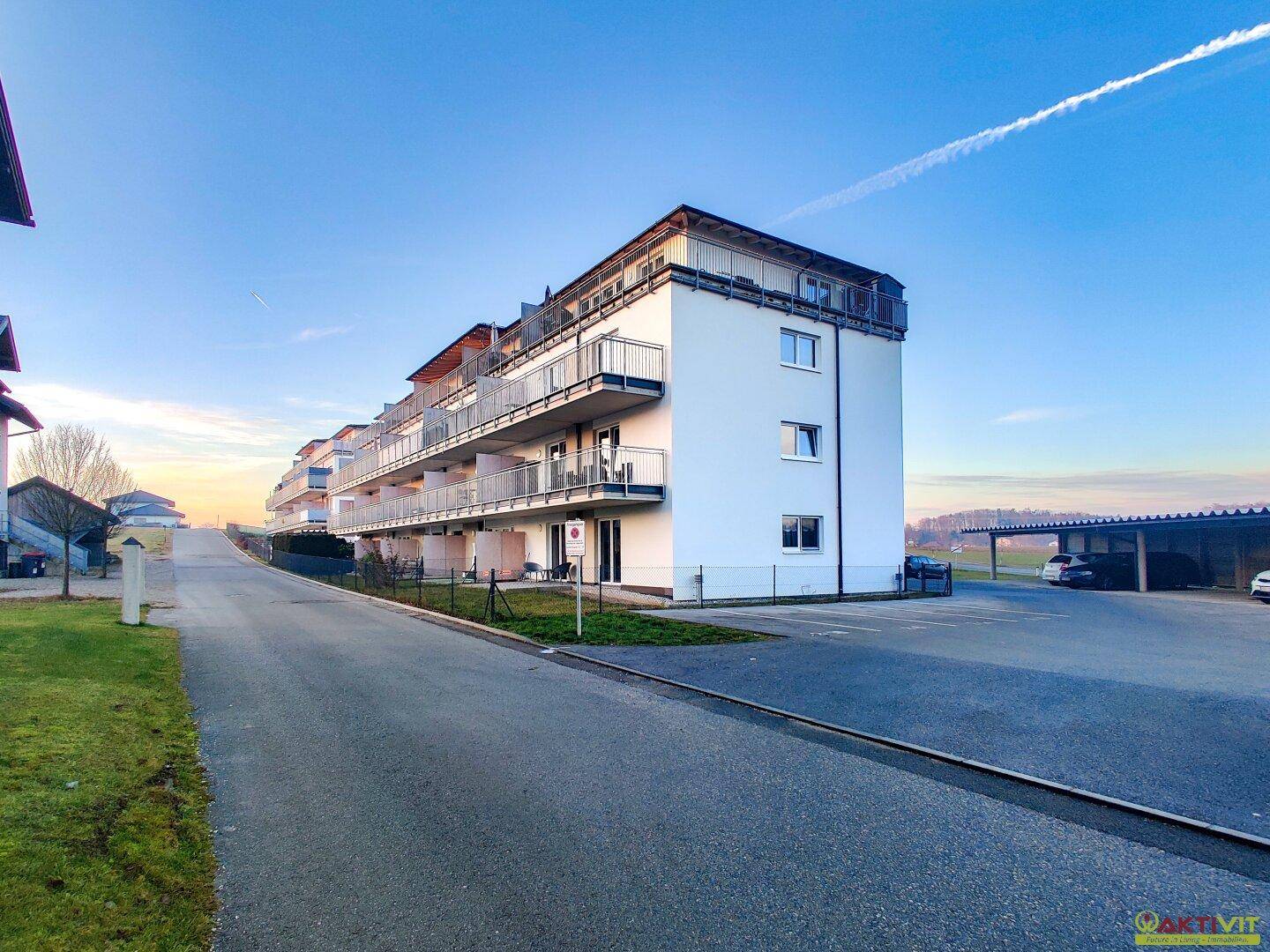Neubau-Wohnanlage in ländlicher Umgebung mit Parkplätzen und weitem Blick in die Ferne.