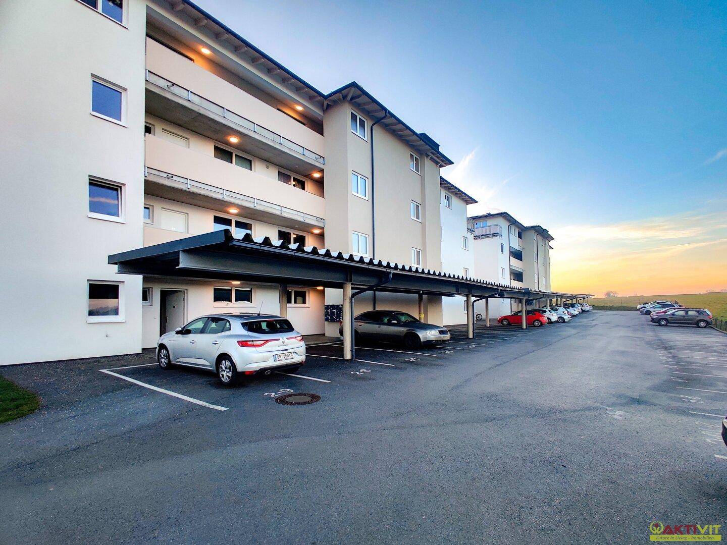 Parkplatz mit Carports vor einer modernen Wohnanlage bei Sonnenuntergang.