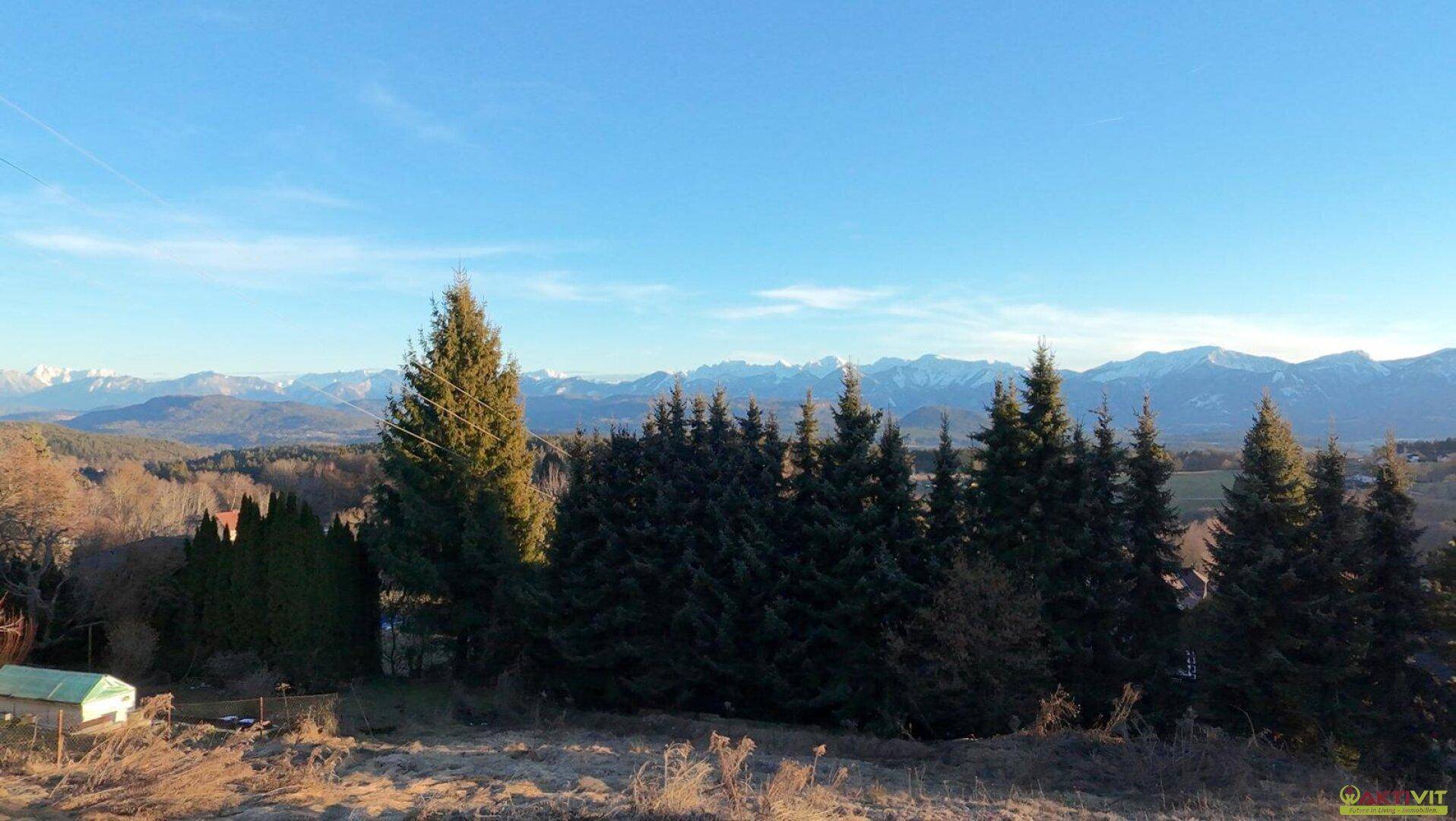 Idyllischer Ausblick auf die Natur mit weiten Feldern, Wäldern und der majestätischen Bergkette im Hintergrund.