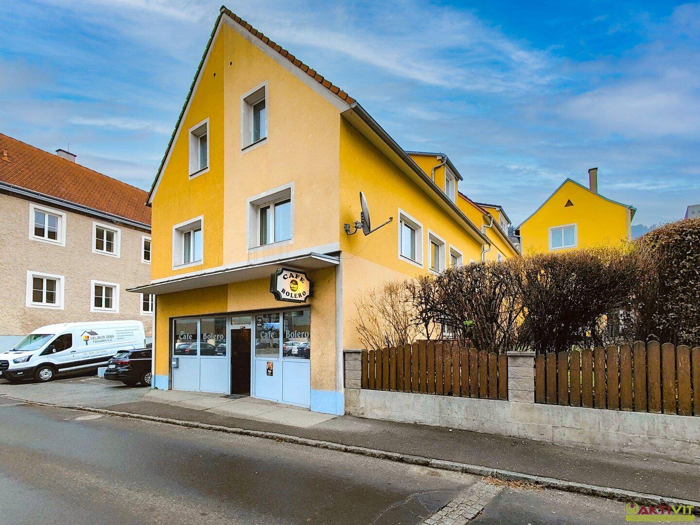 Gelbe Fassade eines Gebäudes mit einem Café im Erdgeschoss und Wohnungen darüber.