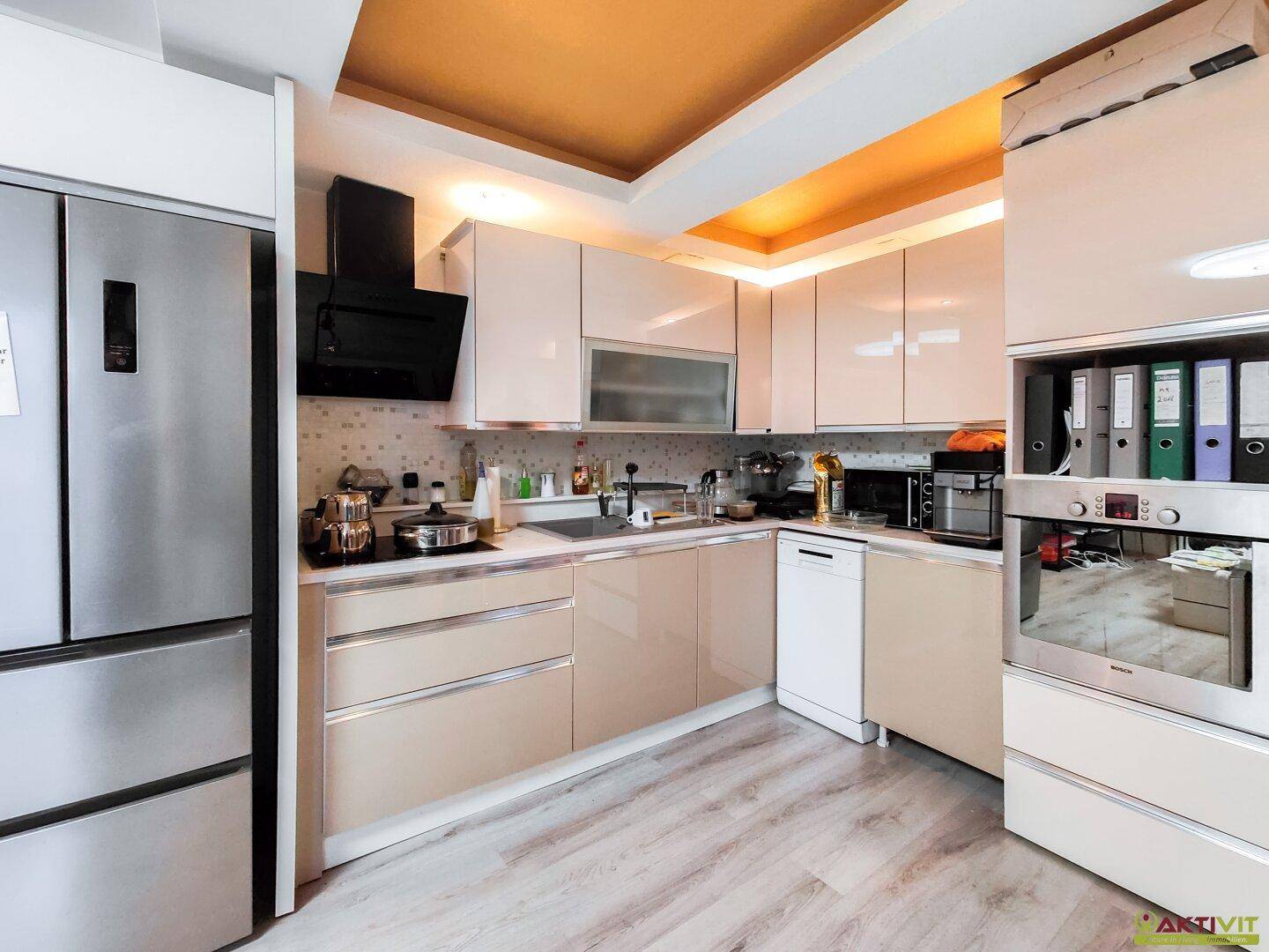 Moderne Küche mit beigefarbenen Hochglanzschränken, integrierten Geräten und Holzoptikboden.