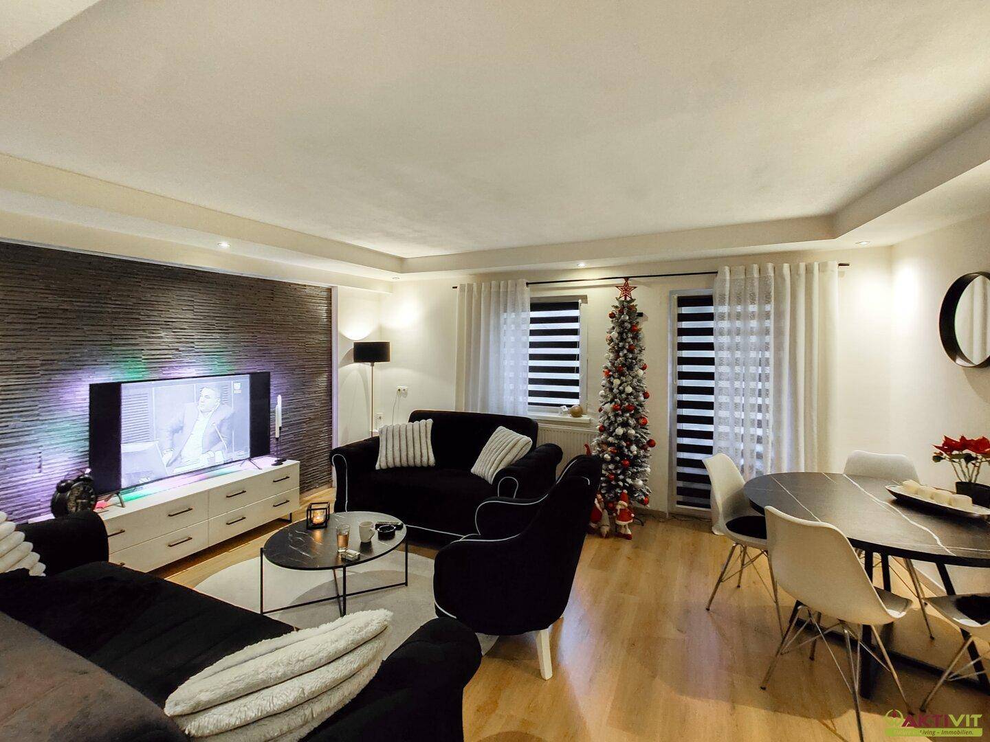 Gemütlicher Wohn-Essbereich mit Holzboden, dunklen Möbeln und einem festlich geschmückten Weihnachtsbaum.