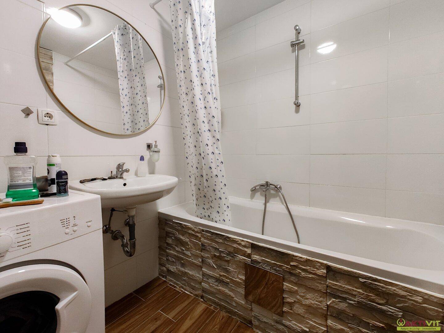 Helles Badezimmer mit Badewanne, Waschmaschine und modernen Fliesen an Wänden und Wanne.