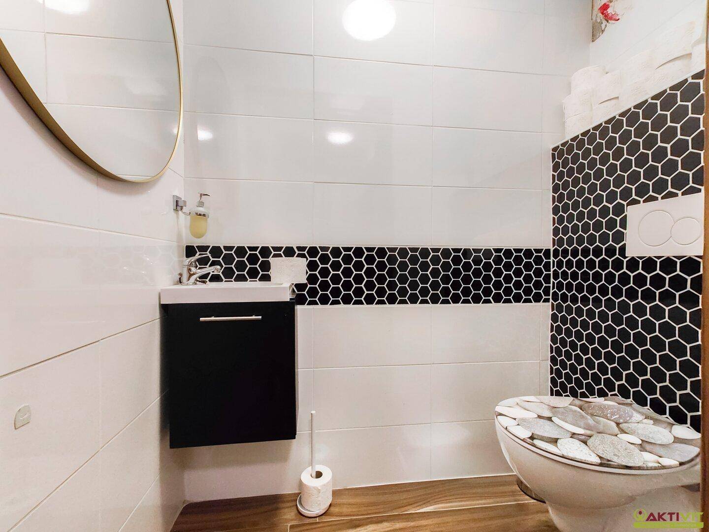 Modernes Gäste-WC mit schwarzen und weißen Fliesen, wandmontierter Toilette und kleinem Waschbecken.