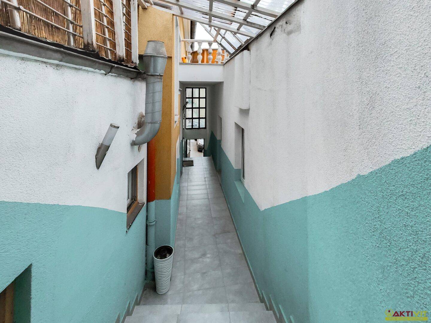 Schmaler Durchgang mit Treppe, zweifarbigen Wänden und Blick auf einen oberen Bereich.