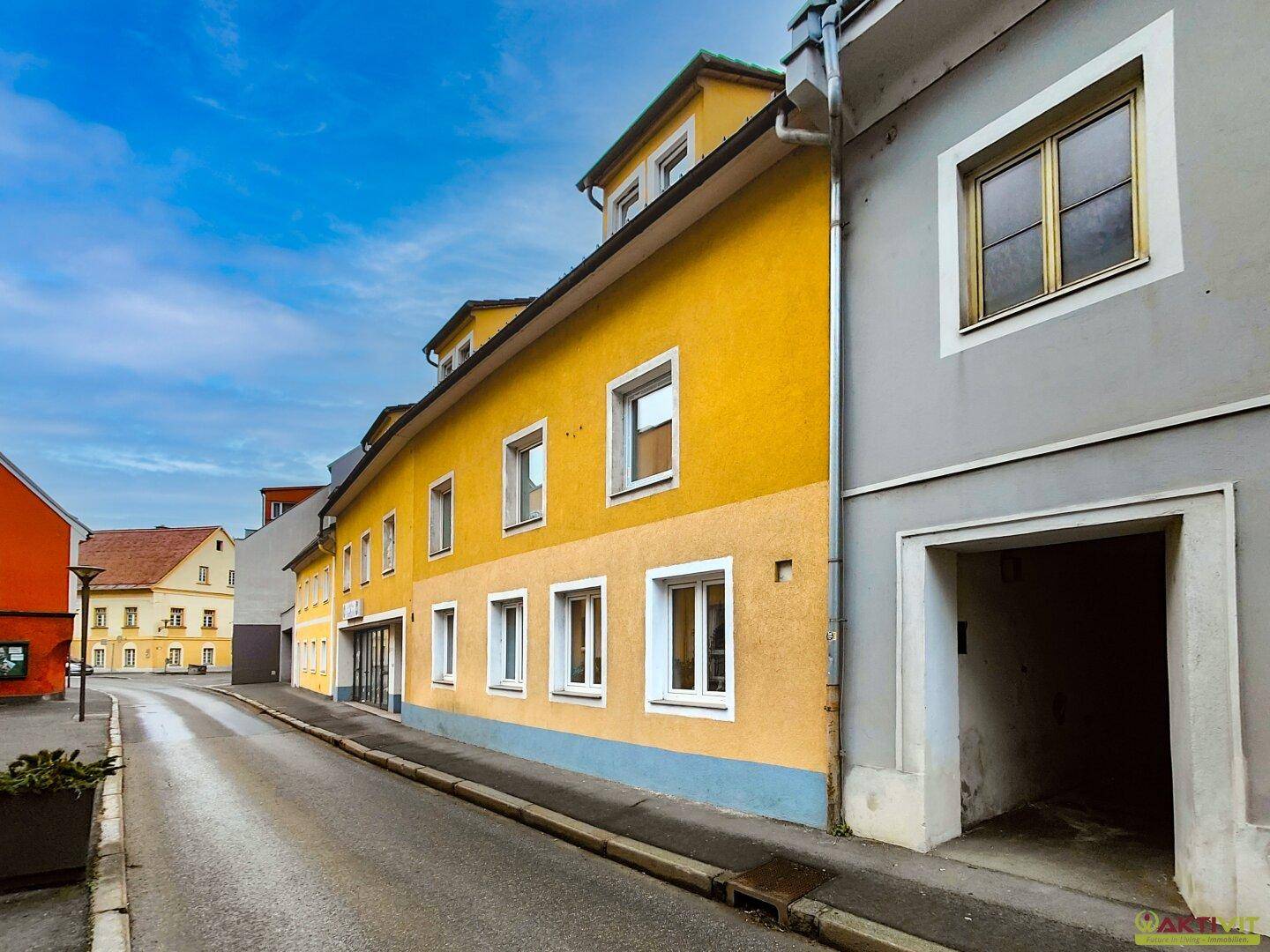 Seitenansicht des gelben Gebäudes an einer ruhigen Straße mit weiteren Häusern im Hintergrund.