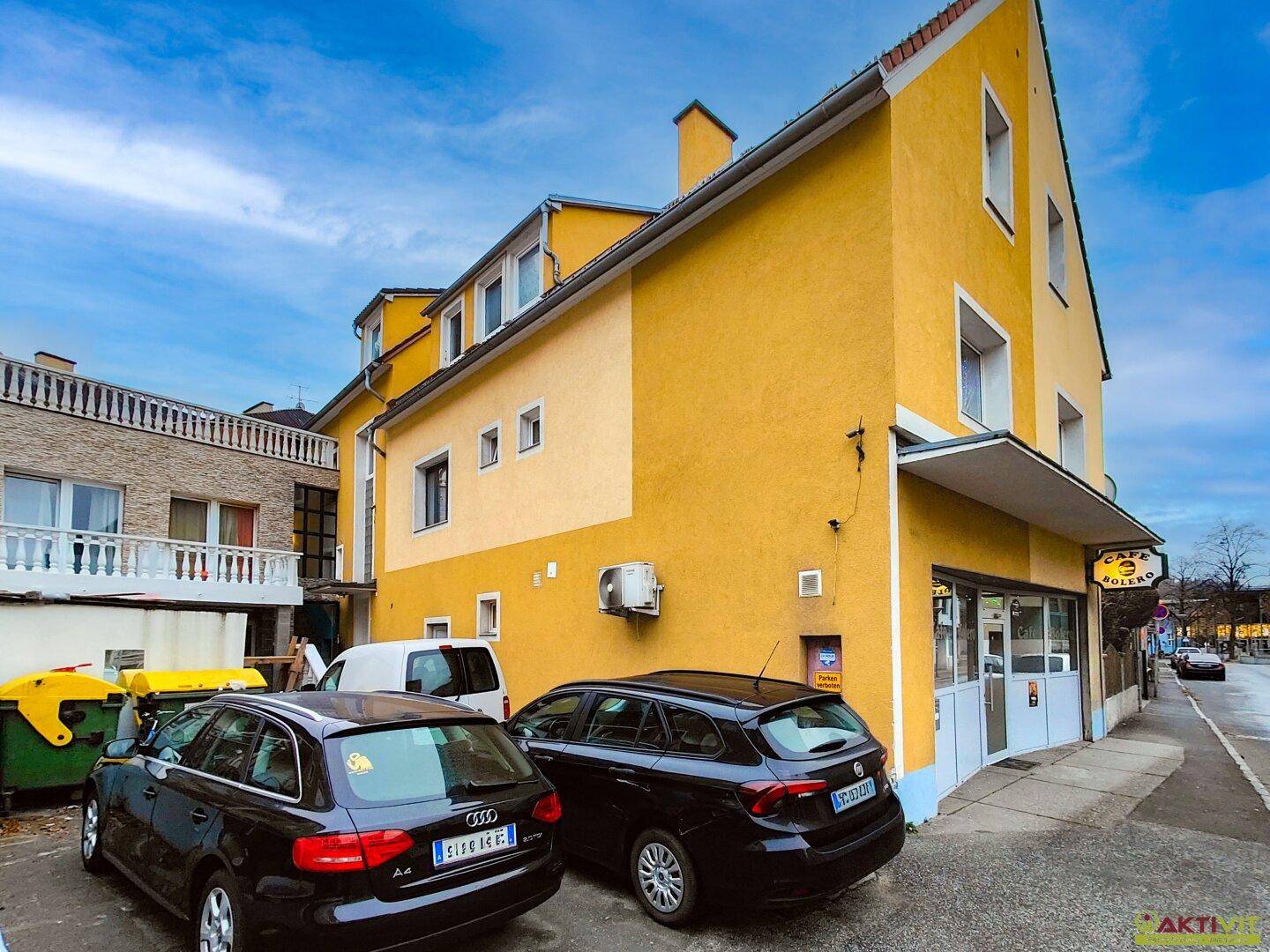 Ecke des gelben Gebäudes mit einem Café im Erdgeschoss und geparkten Autos davor.