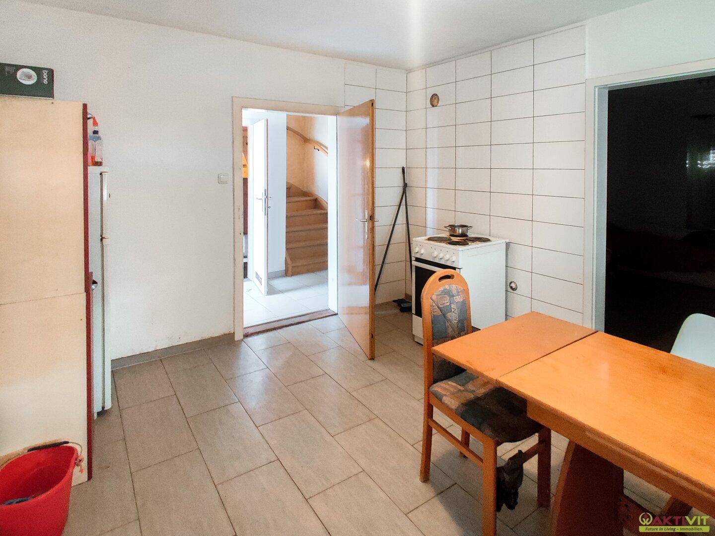 Einfache Küche mit Fliesenboden, Herd und Zugang zum Treppenhaus.