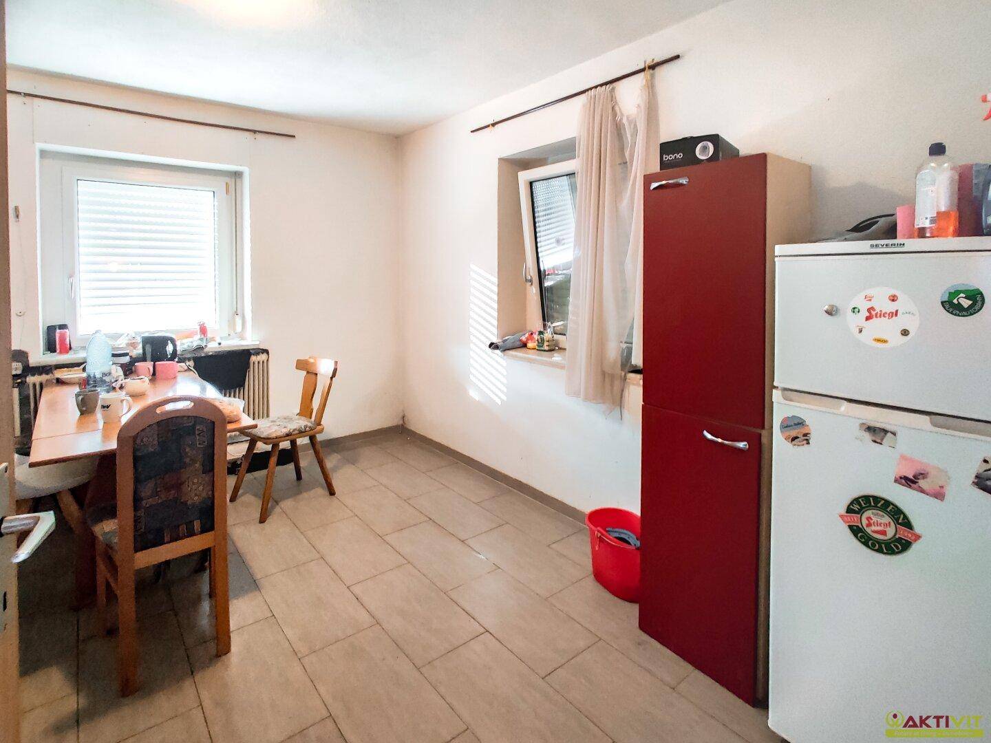 Essbereich in der Küche mit Tisch, Stühlen und Kühlschrank, gut beleuchtet durch Fenster.