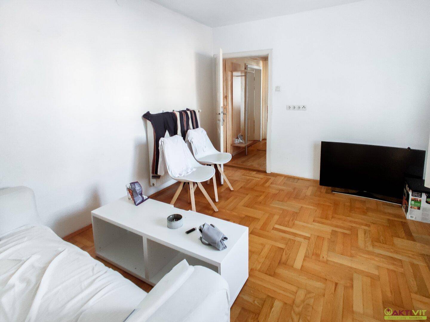 Wohnzimmer mit Fischgrätparkettboden, weißem Sofa und Blick in den Flur.