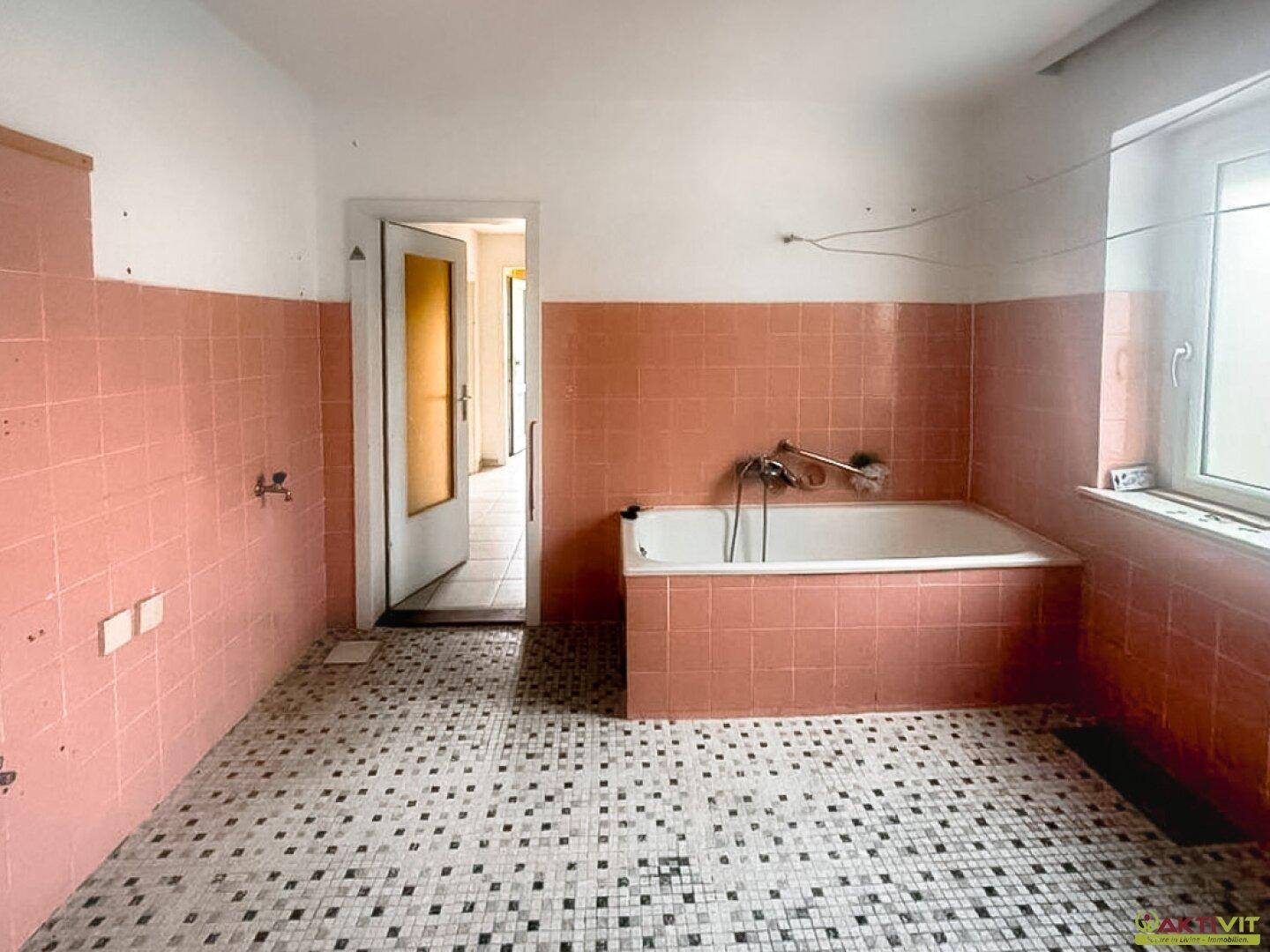 Badezimmer in Renovierungsbedarf mit rosa Fliesen, Badewanne und Fenster.