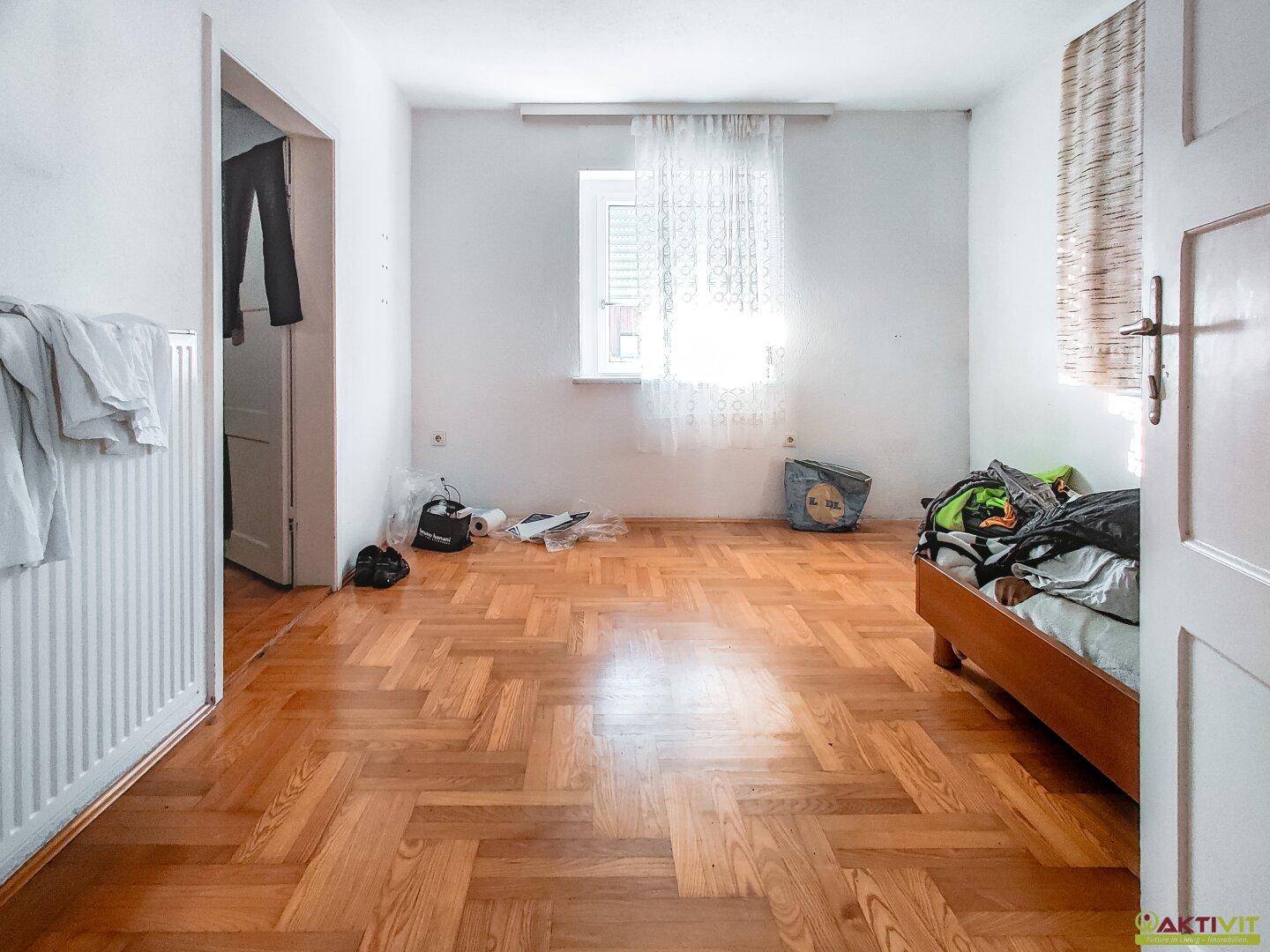 Schlafzimmer mit Fischgrätparkettboden, Fenster und viel natürlichem Licht.