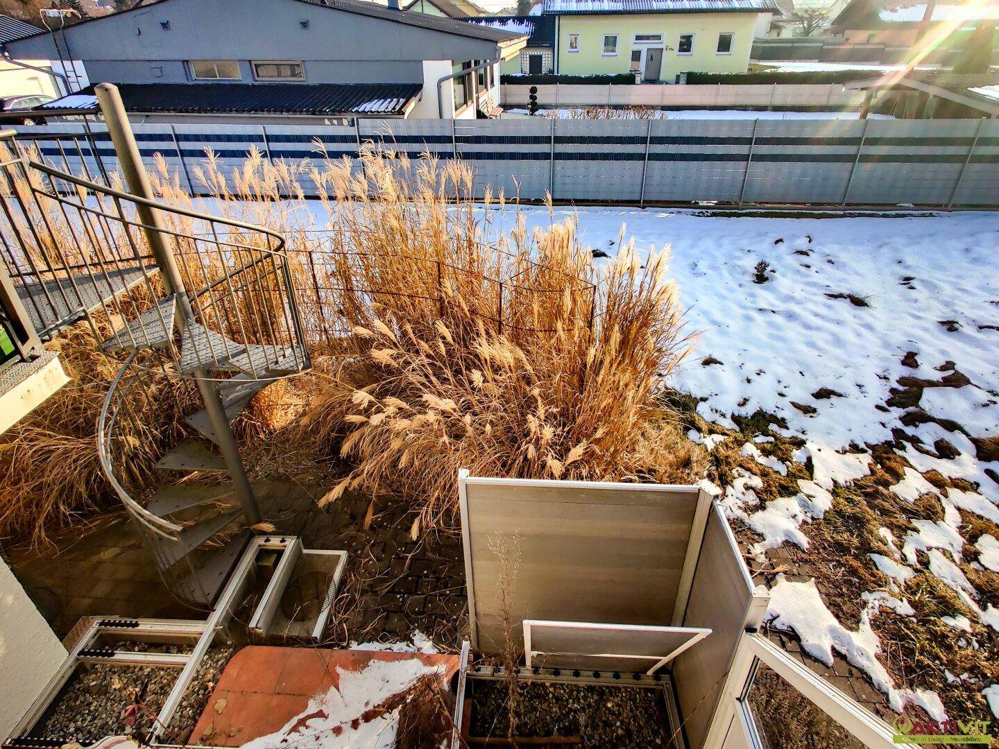 Gartenbereich mit Ziergräsern, Schnee und einer Wendeltreppe zum oberen Stockwerk.