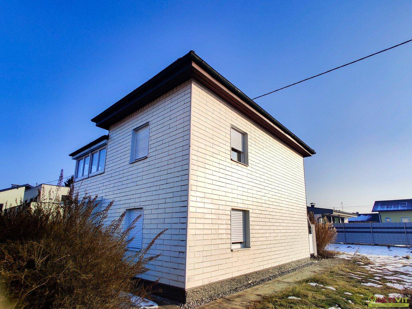 Seitenansicht des Hauses mit weißer Ziegelfassade und Fenstern mit Rollläden.