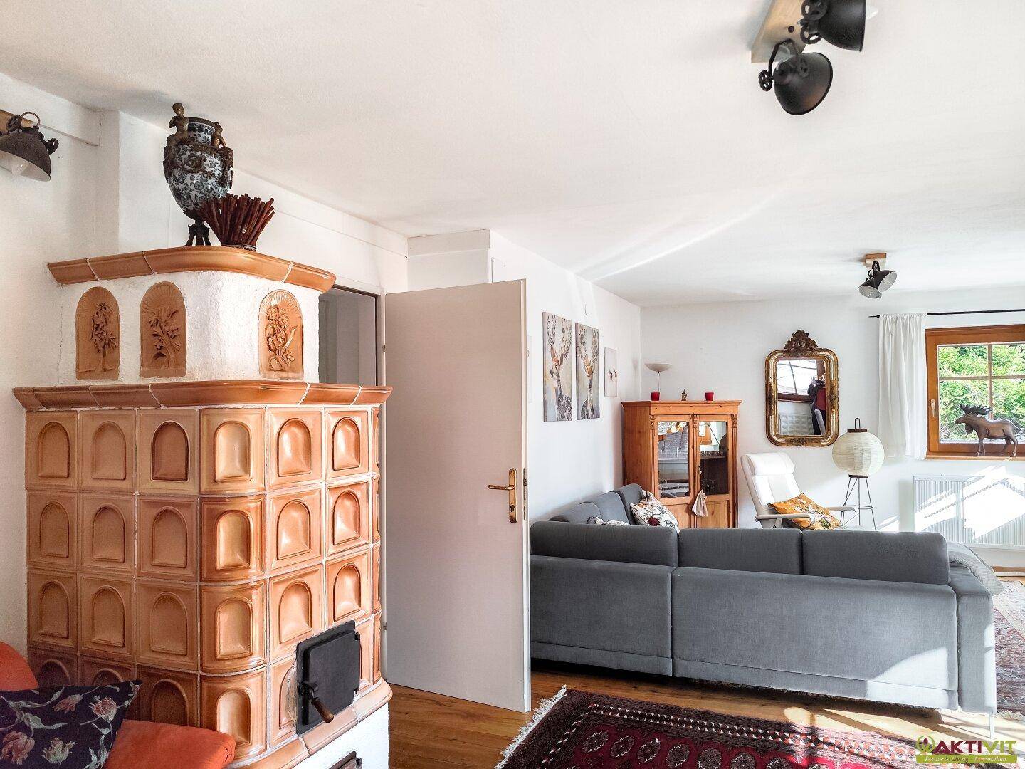 Heller Wohnbereich mit großem Kachelofen und bequemer Couch, ideal zum Entspannen.