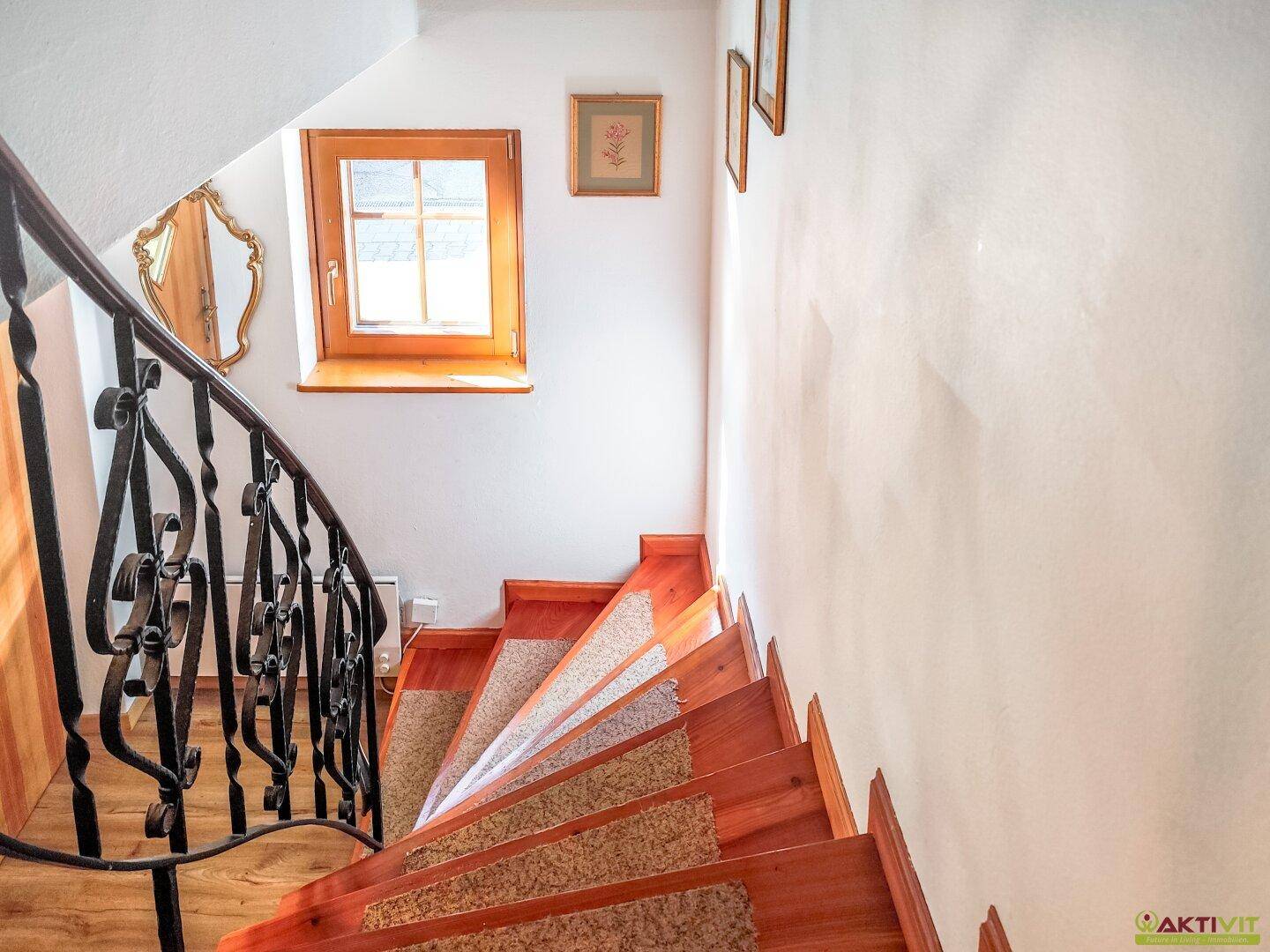 Holztreppe mit schmiedeeisernem Geländer und Fenster, das natürliches Licht hereinlässt.