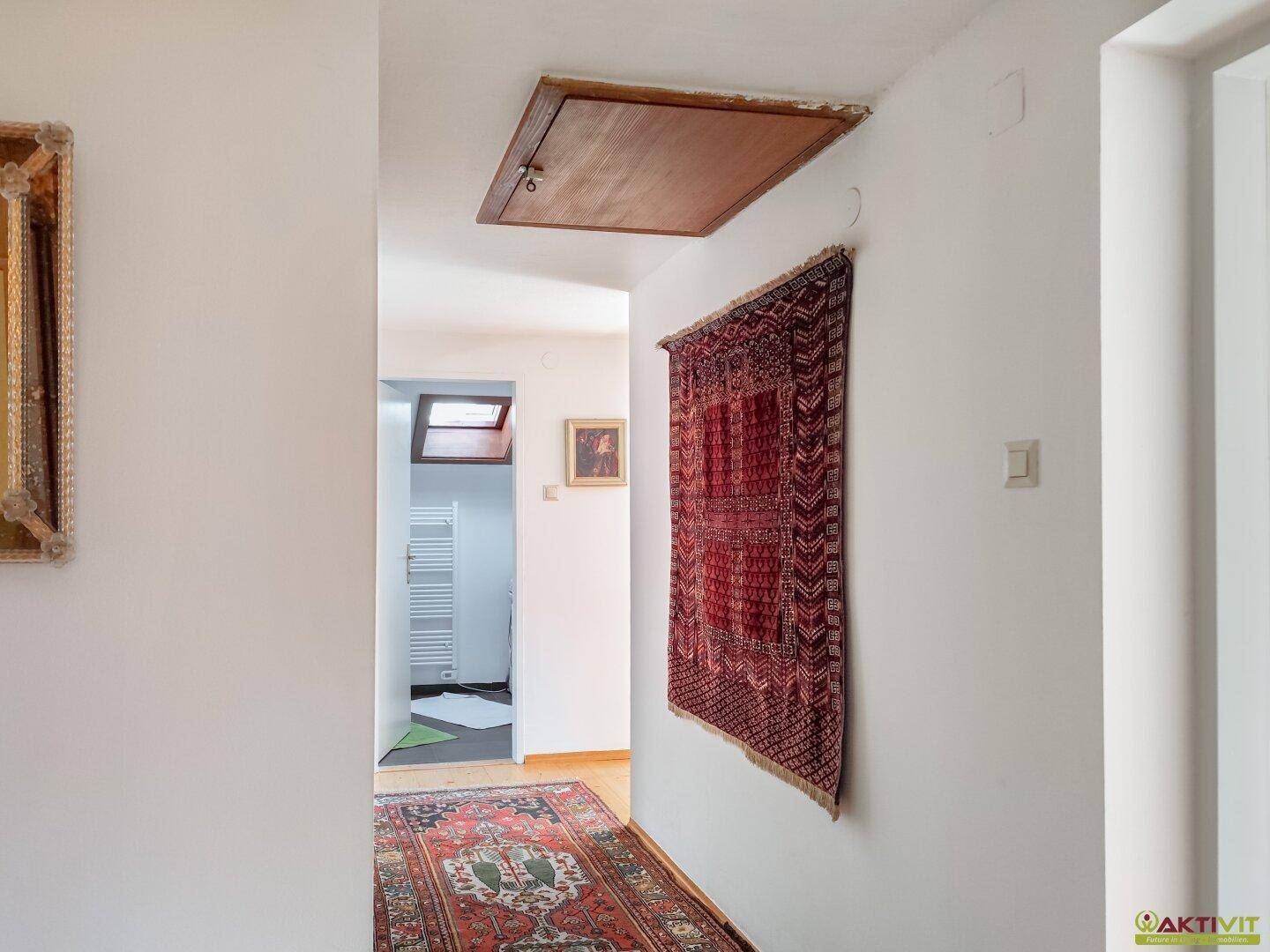 Heller Flur mit Teppich und Zugang zu einem Dachboden, geschmückt mit einem Wandteppich.