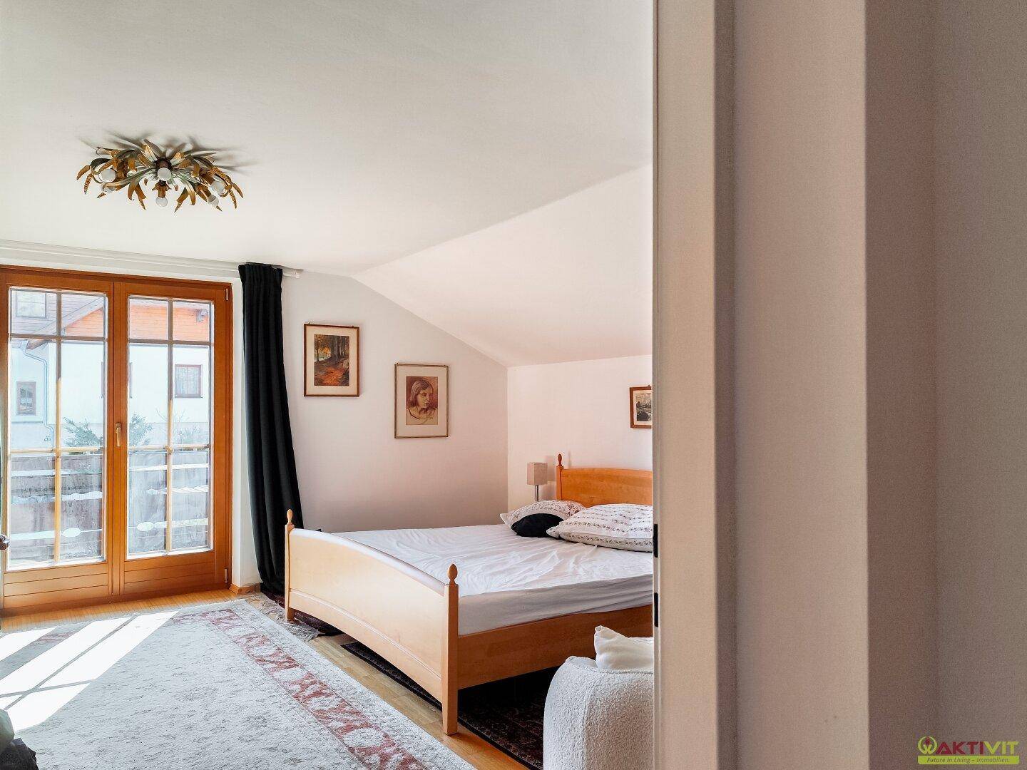Schlafzimmer im Dachgeschoss mit Holzbett, schrägen Decken und Balkonzugang.