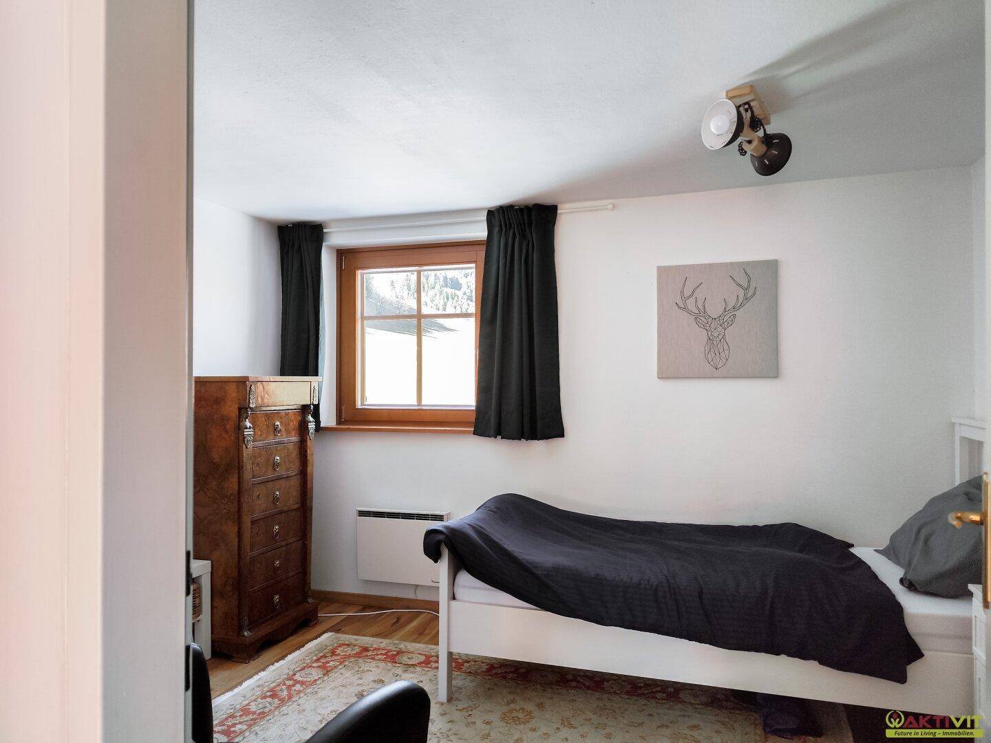 Helles Schlafzimmer mit Einzelbett, Holzkommode und Fenster mit Bergblick.