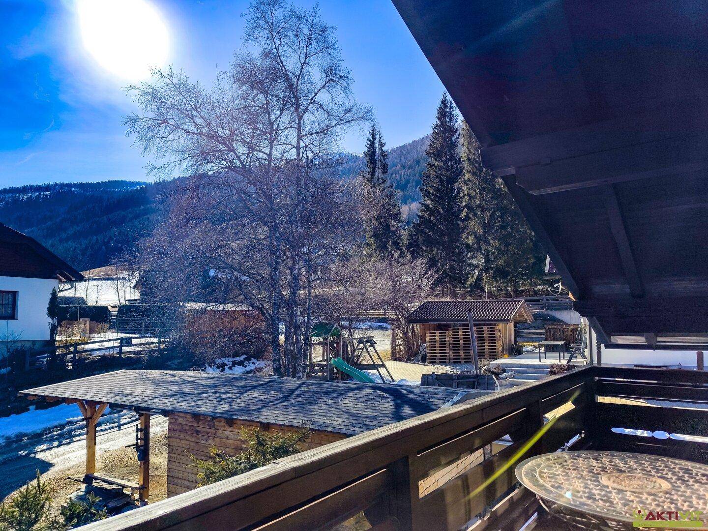 Sonniger Balkon mit Sitzgelegenheiten und Blick auf die umliegende Berglandschaft.