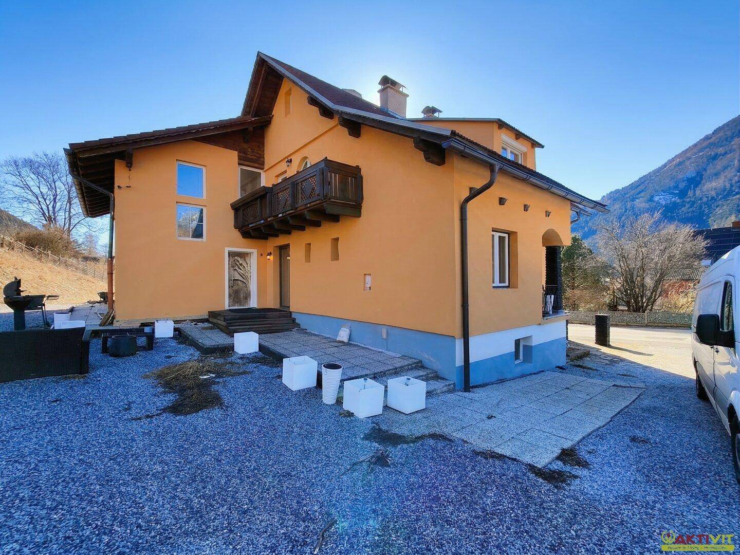 Rückseite des Hauses mit Kiesfläche, gepflastertem Bereich und Bergblick.