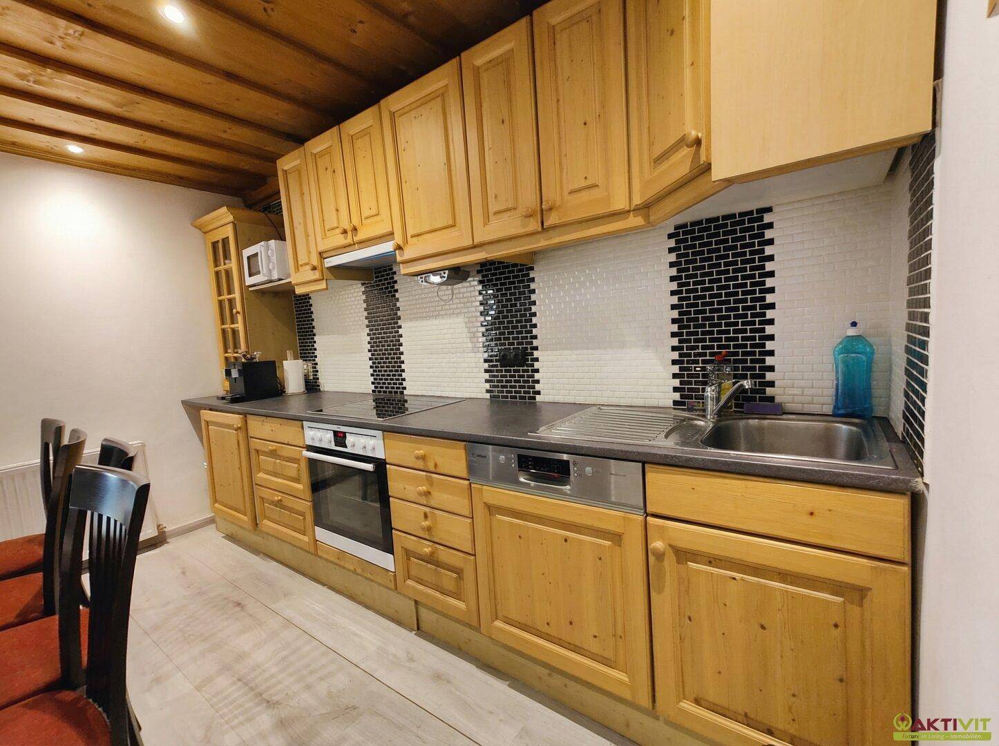 Funktionale Küche mit Holzschränken, Fliesenrückwand und modernen Geräten.